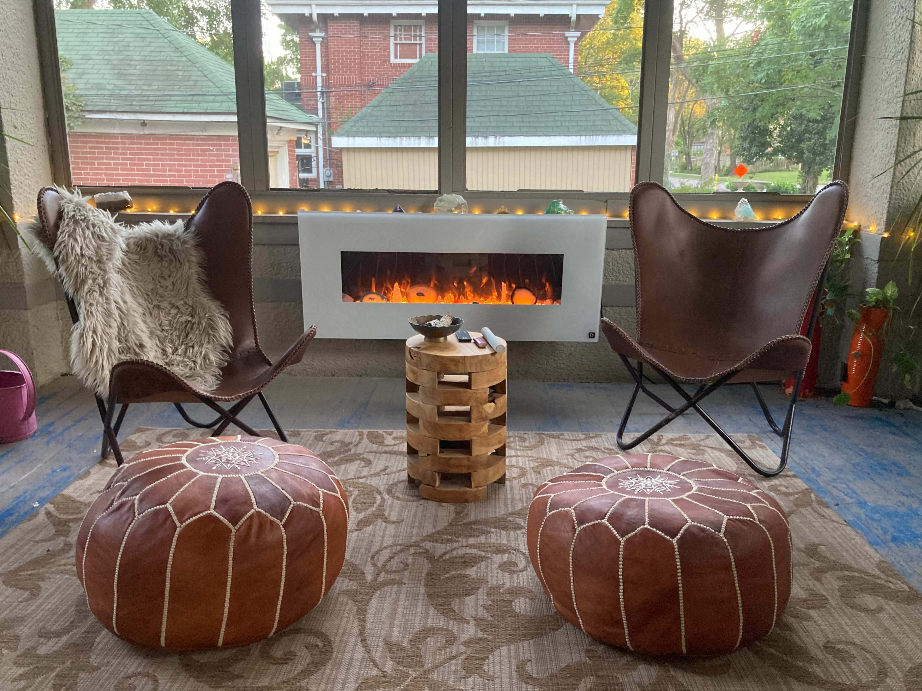 The image shows a cozy sunroom featuring two butterfly chairs, a wooden table, and a modern fireplace, with warm lighting in the background.