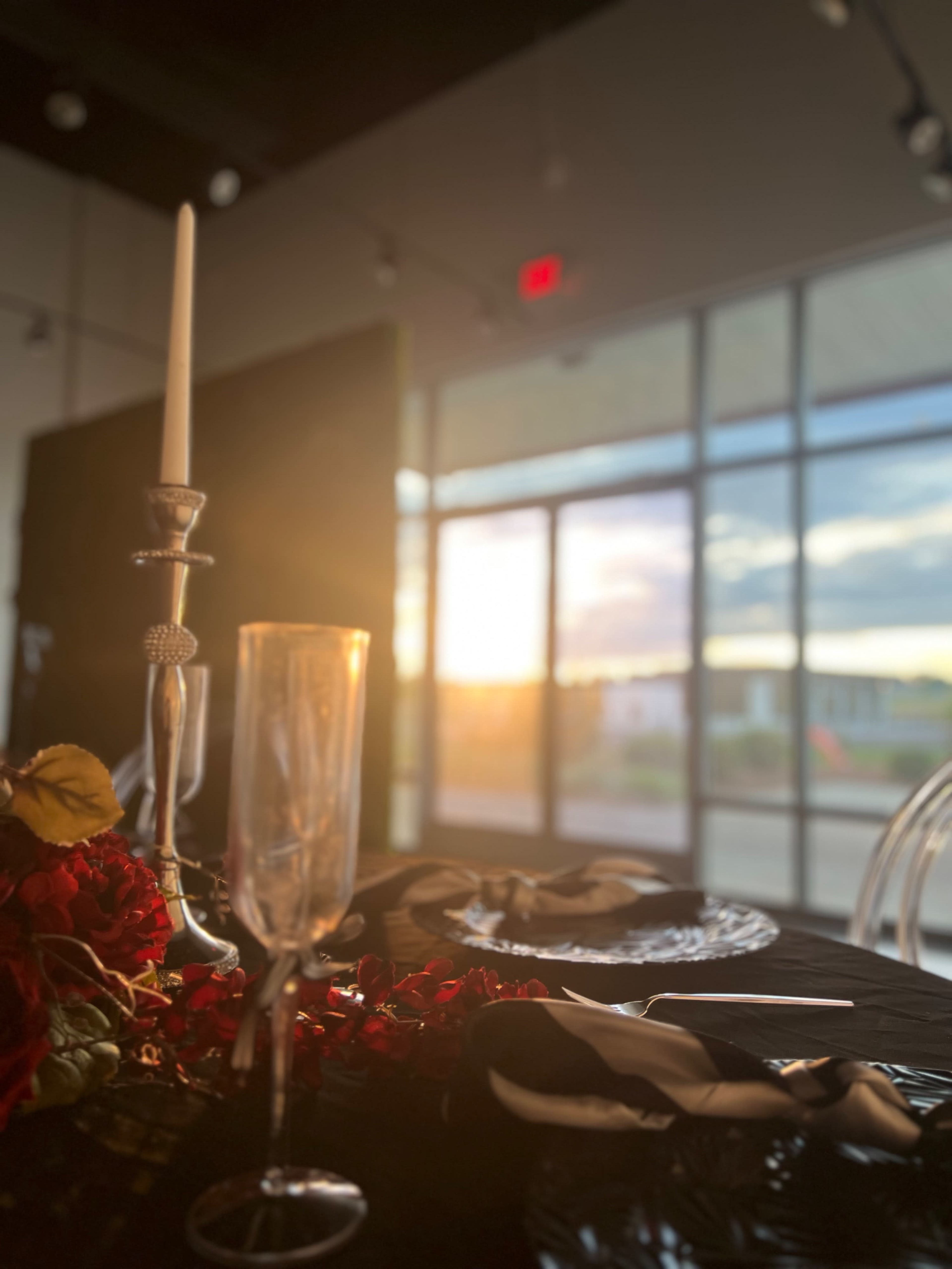 The image shows a beautifully set dining table with a candle and glassware, framed by large windows that let in the warm light of a setting sun.