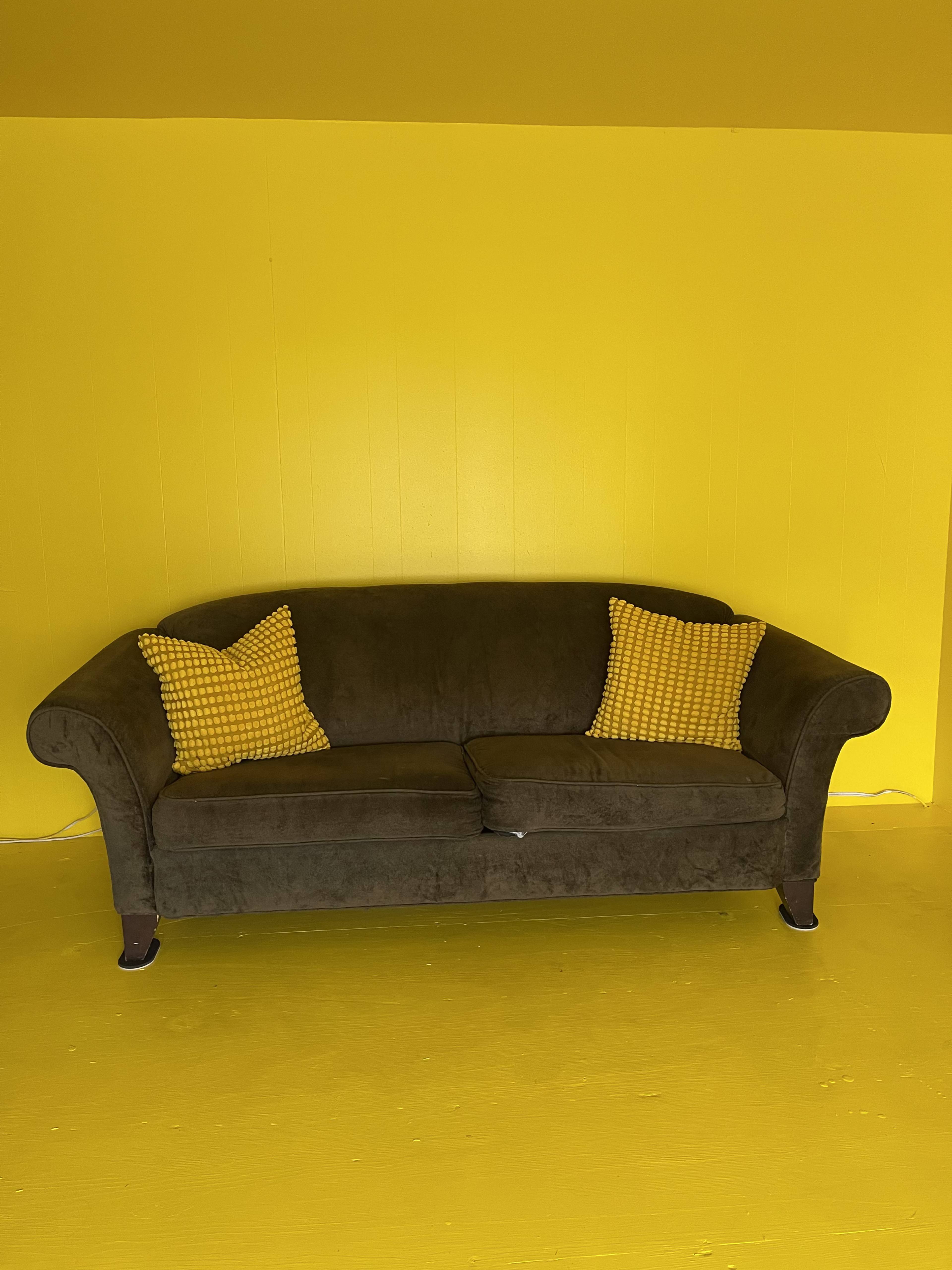 A brown couch with yellow checkered pillows sits on a yellow floor in a brightly colored room.
