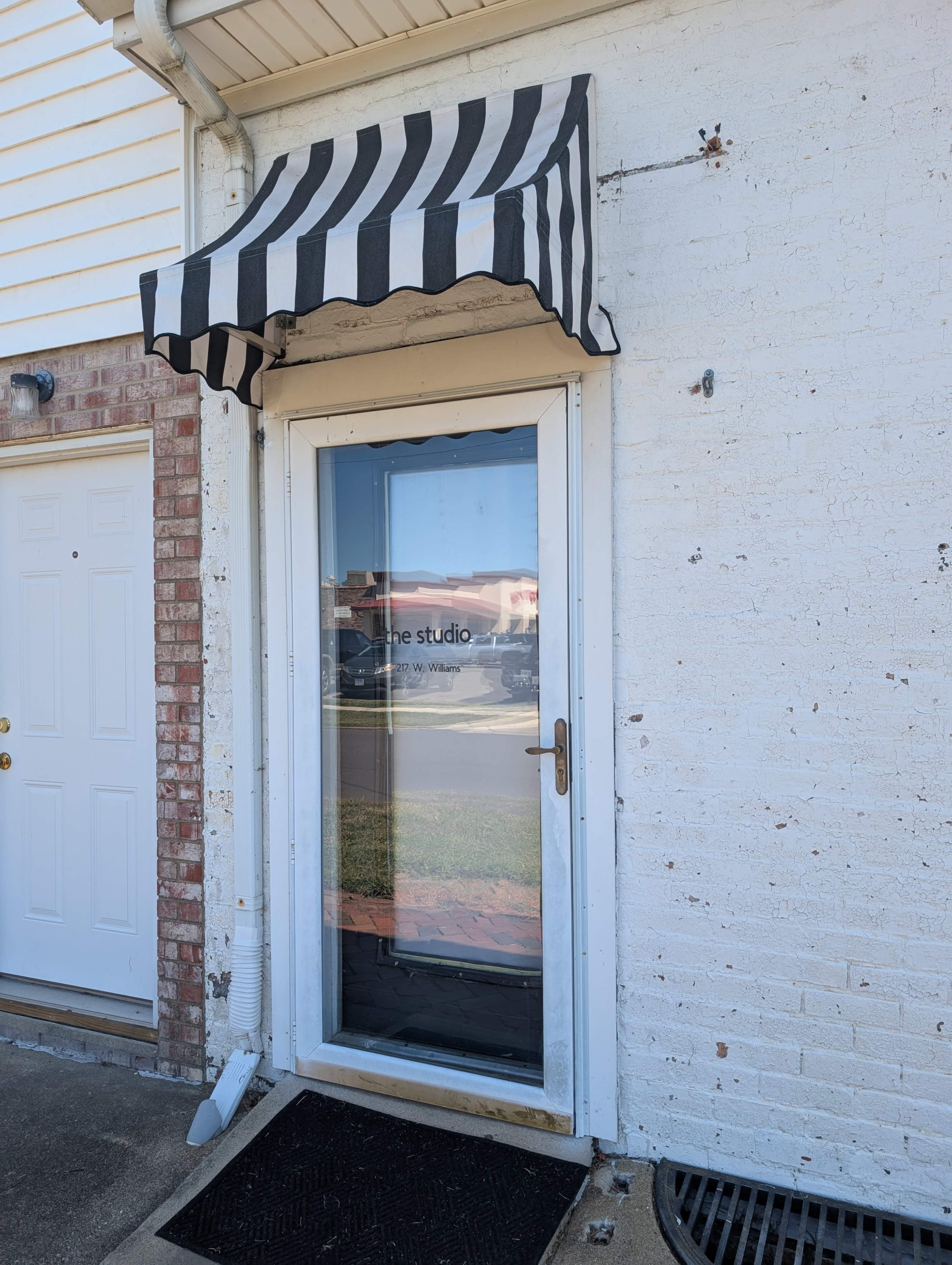 The image shows a storefront entrance with a black and white striped awning and a clear glass door displaying the words "the studio."