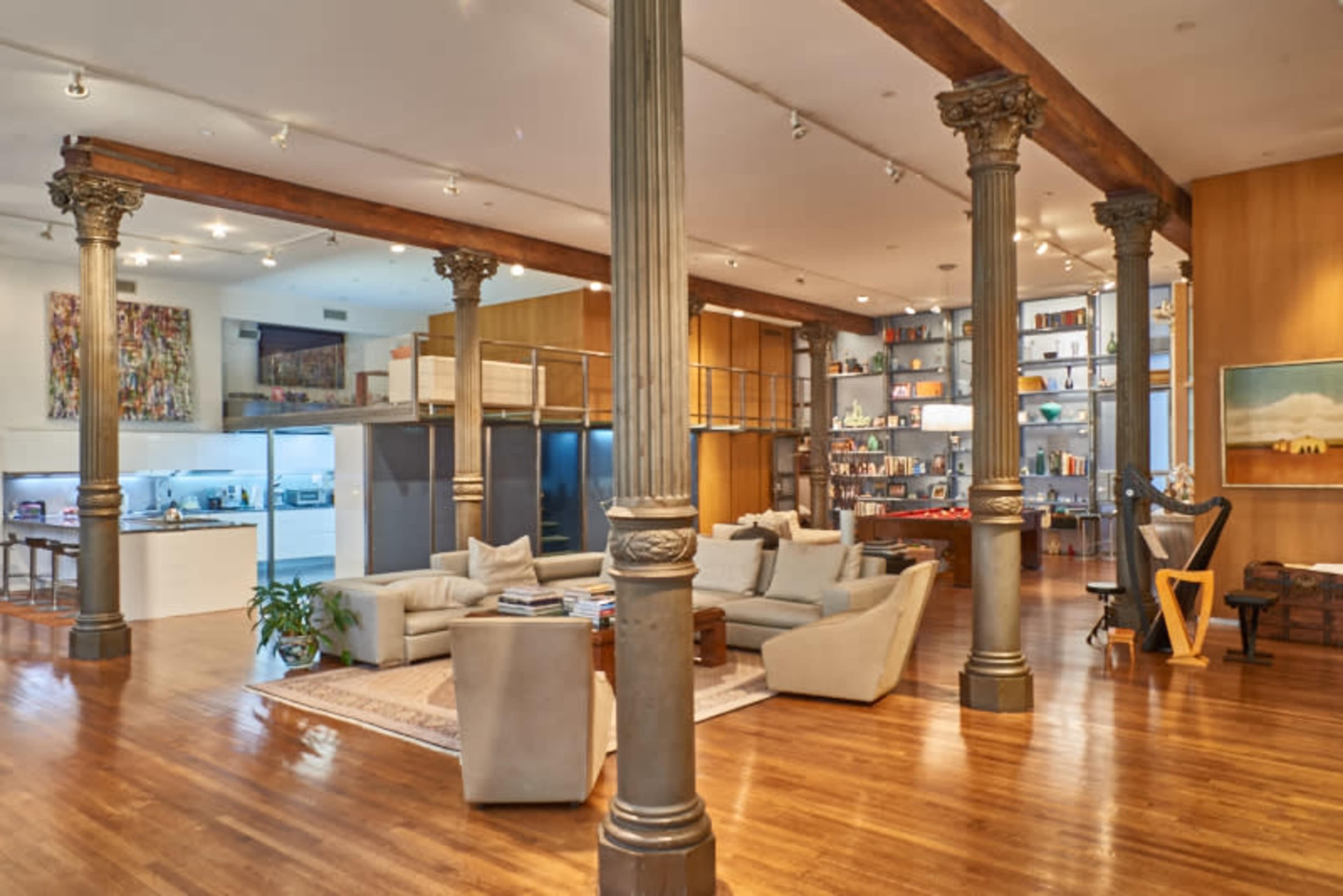 An open-concept living space features modern furnishings, tall columns, and a well-organized bookshelf against a wooden wall.