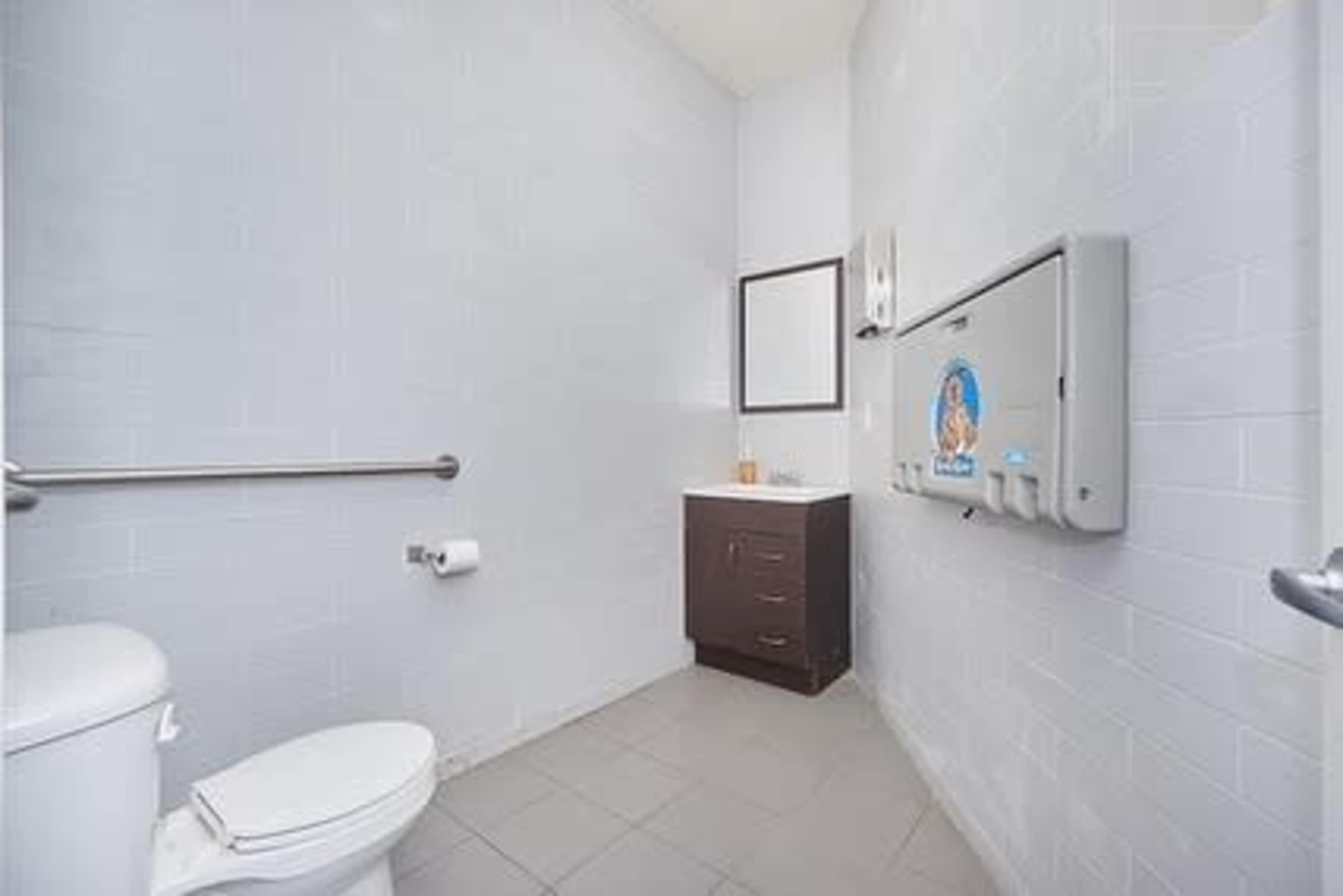 The image shows a small restroom with a toilet, a sink with a mirror above it, and a paper towel dispenser on the wall.