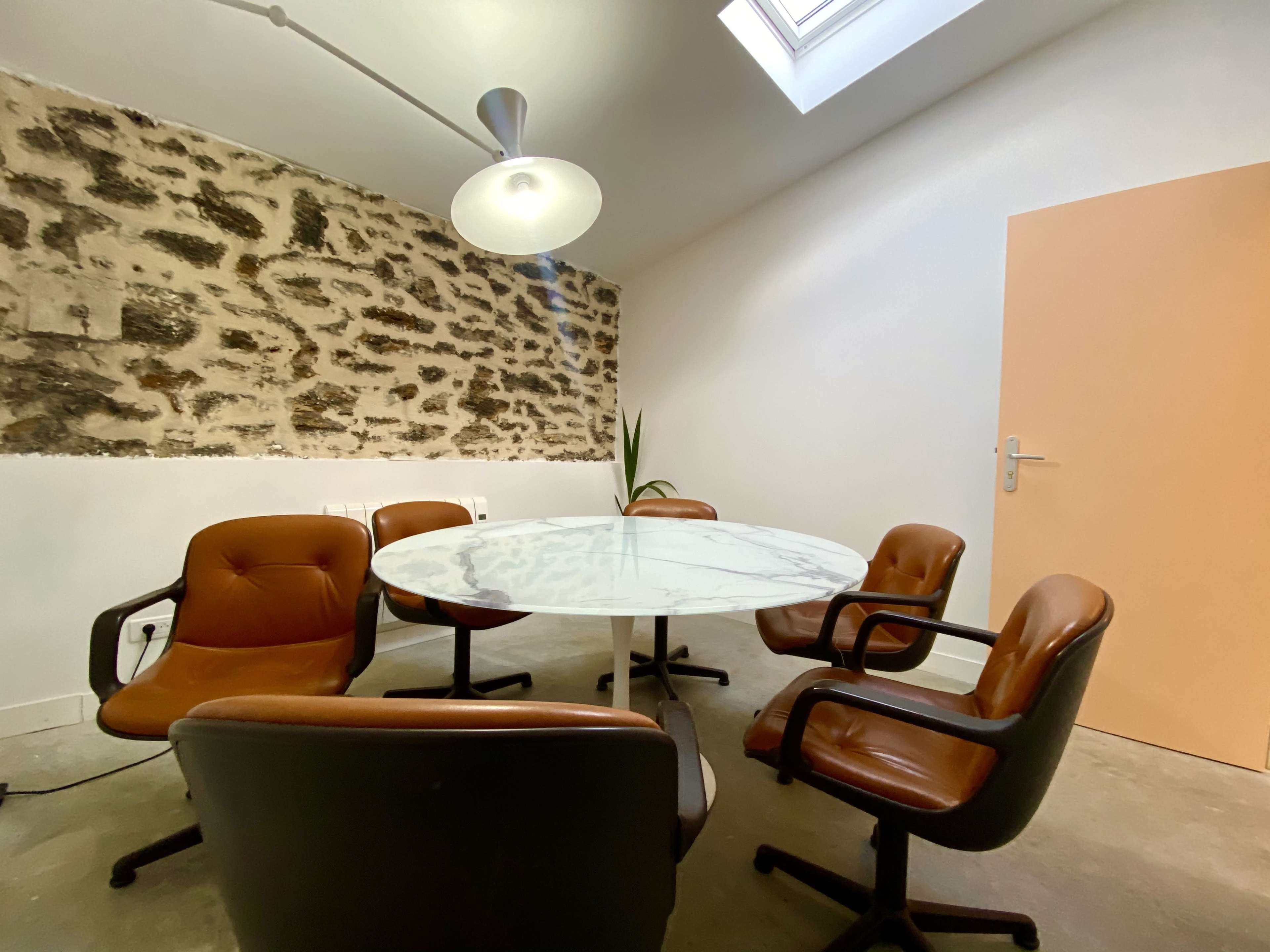 A conference room features a round marble table surrounded by brown chairs and a stone accent wall.