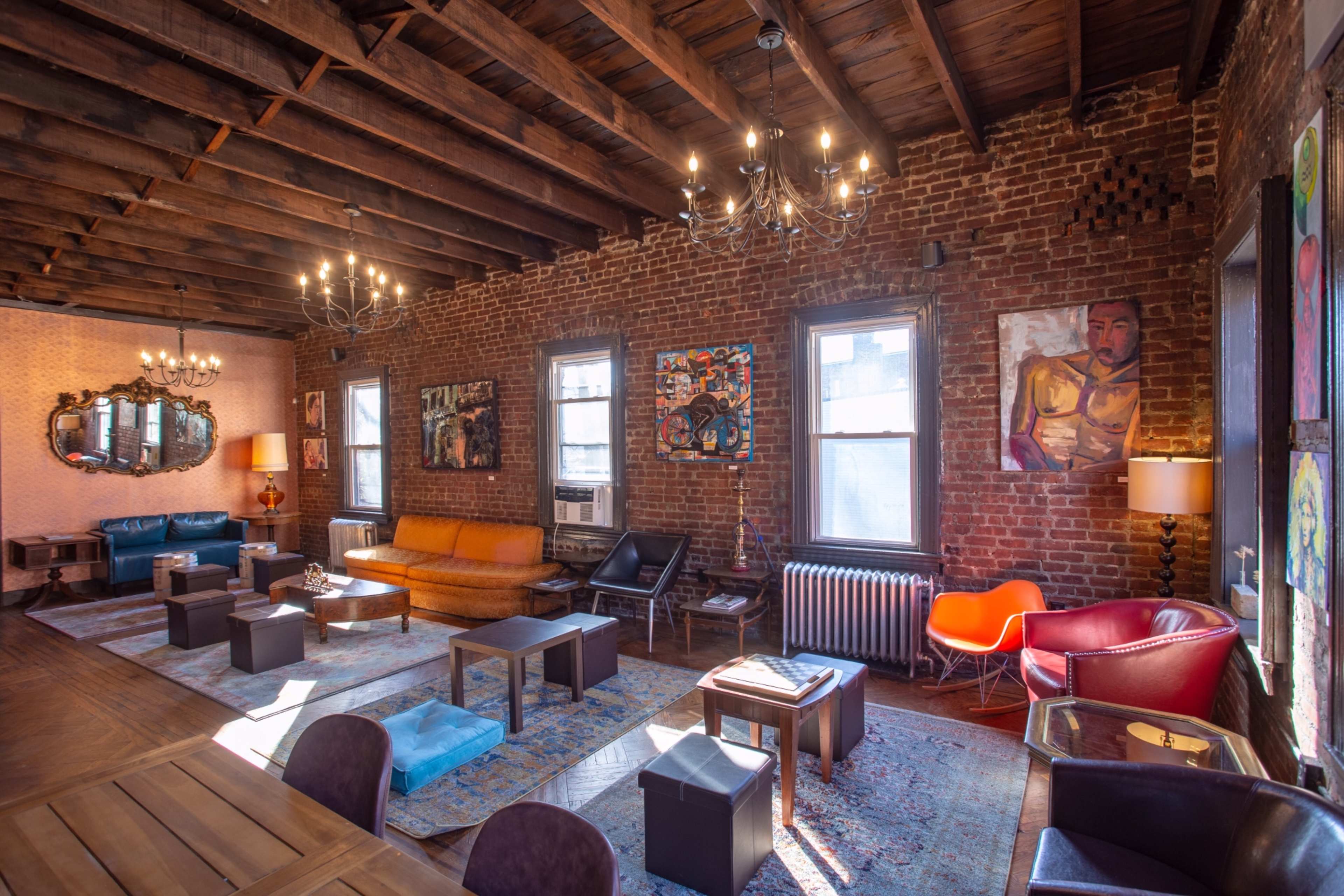 A spacious living room with exposed brick walls, wooden beams, and various seating arrangements, including a blue couch, an orange sofa, and a red chair.