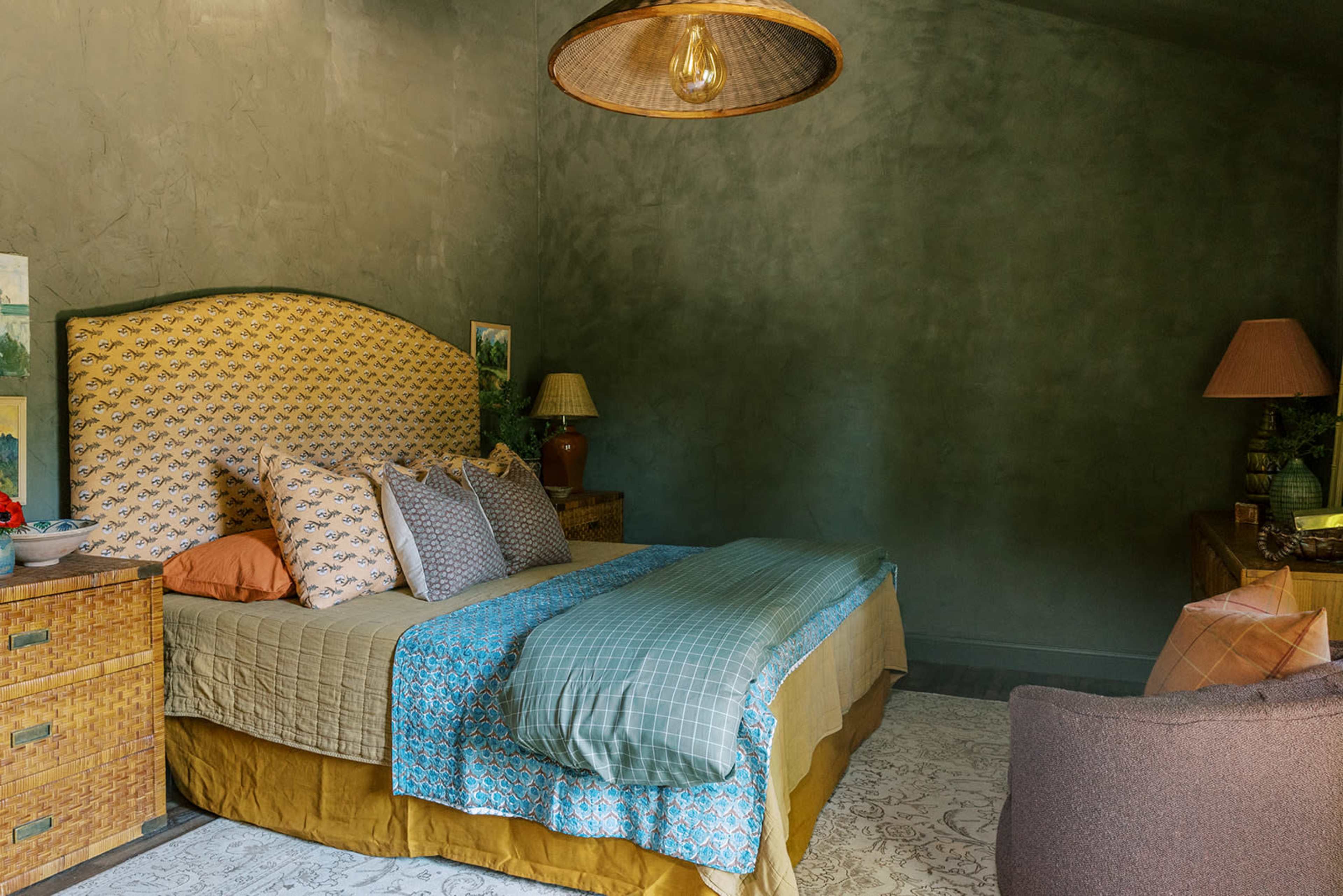A bedroom with a large bed featuring patterned bedding, two bedside lamps, and a textured green wall.