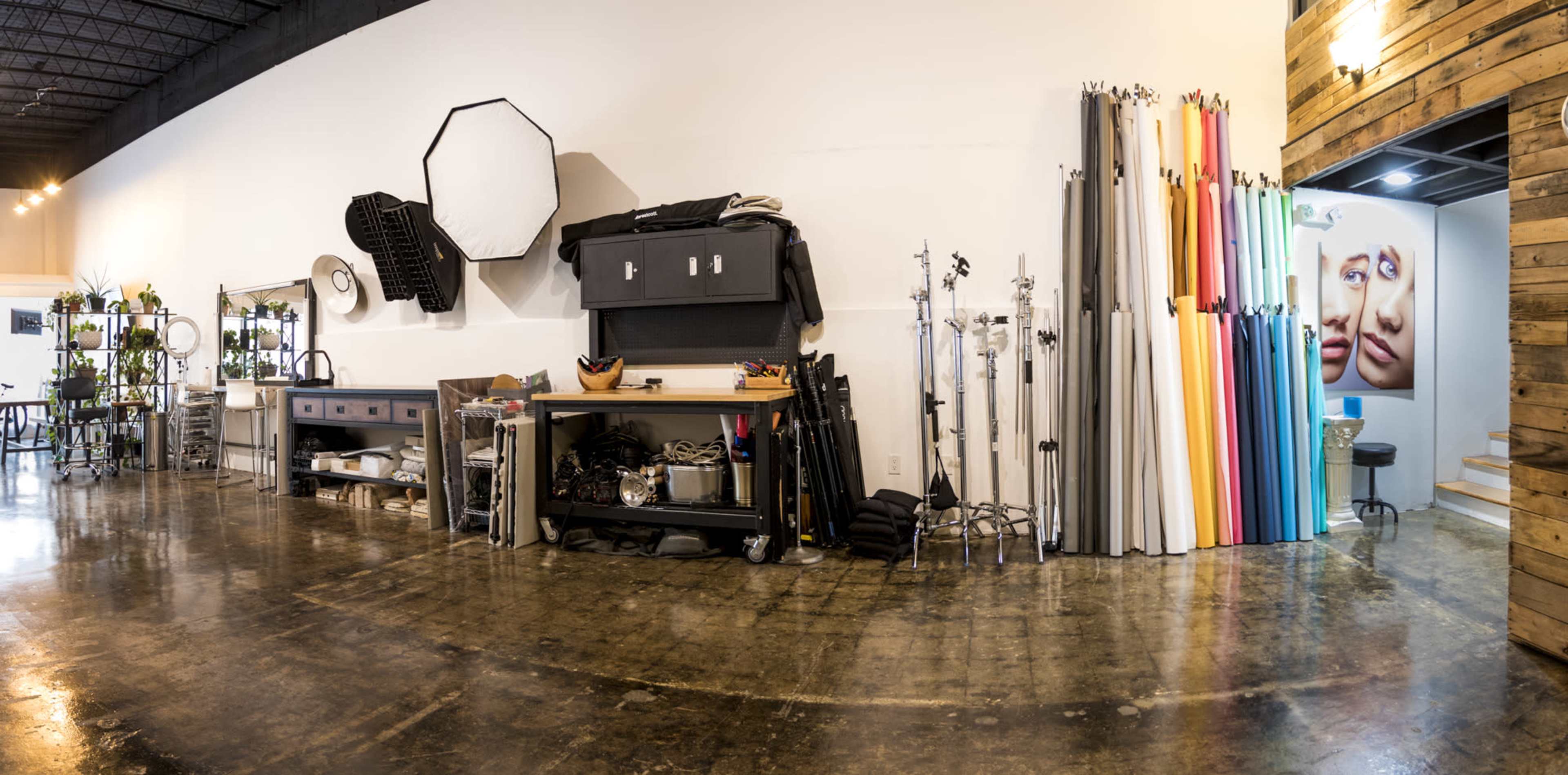 A spacious studio with various photography equipment, including backdrops and lights, arranged along the walls and a large mural of two faces in the background.