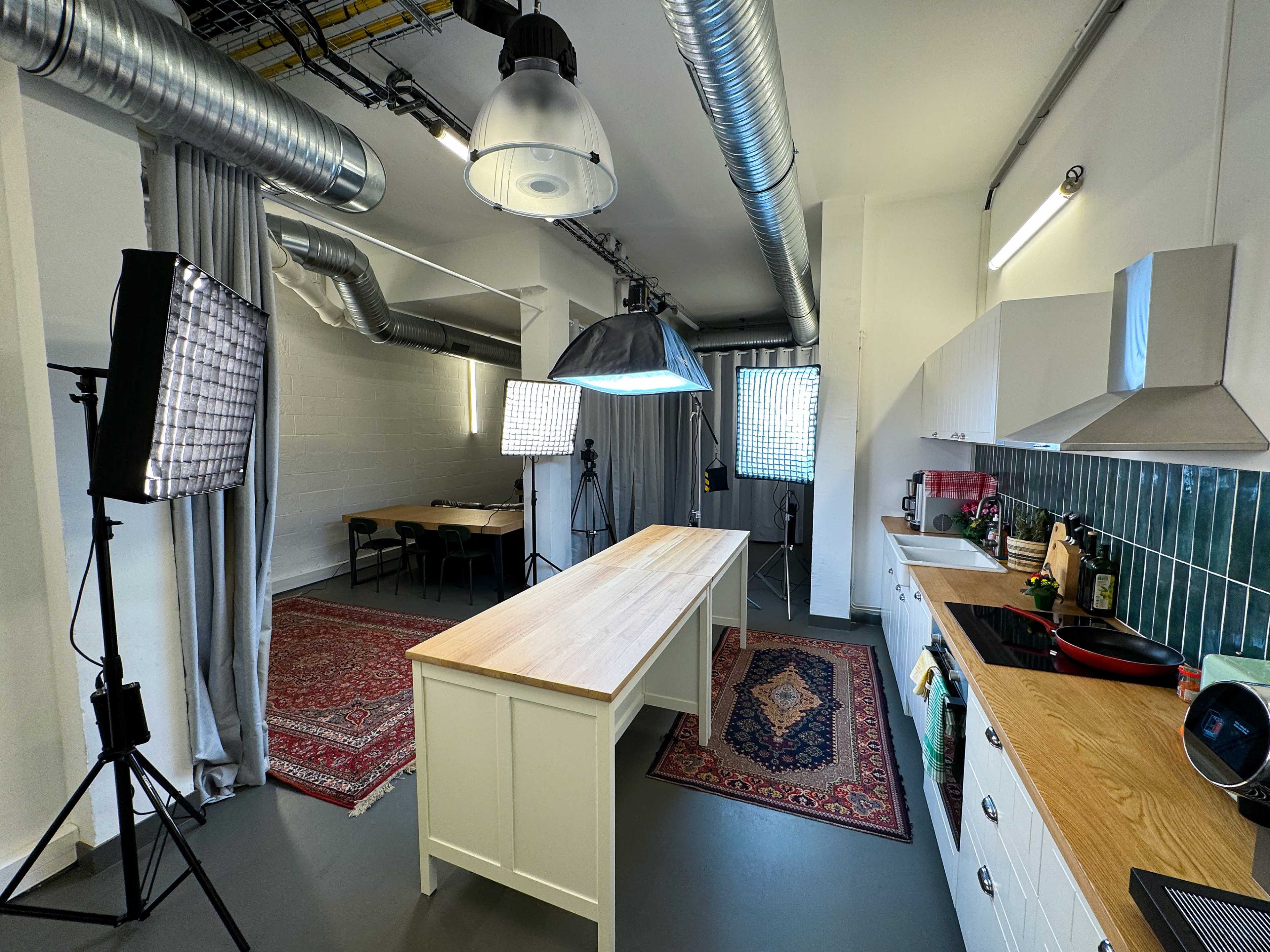 A modern kitchen with a large wooden island, pendant lighting, and professional photography equipment set up in the background.