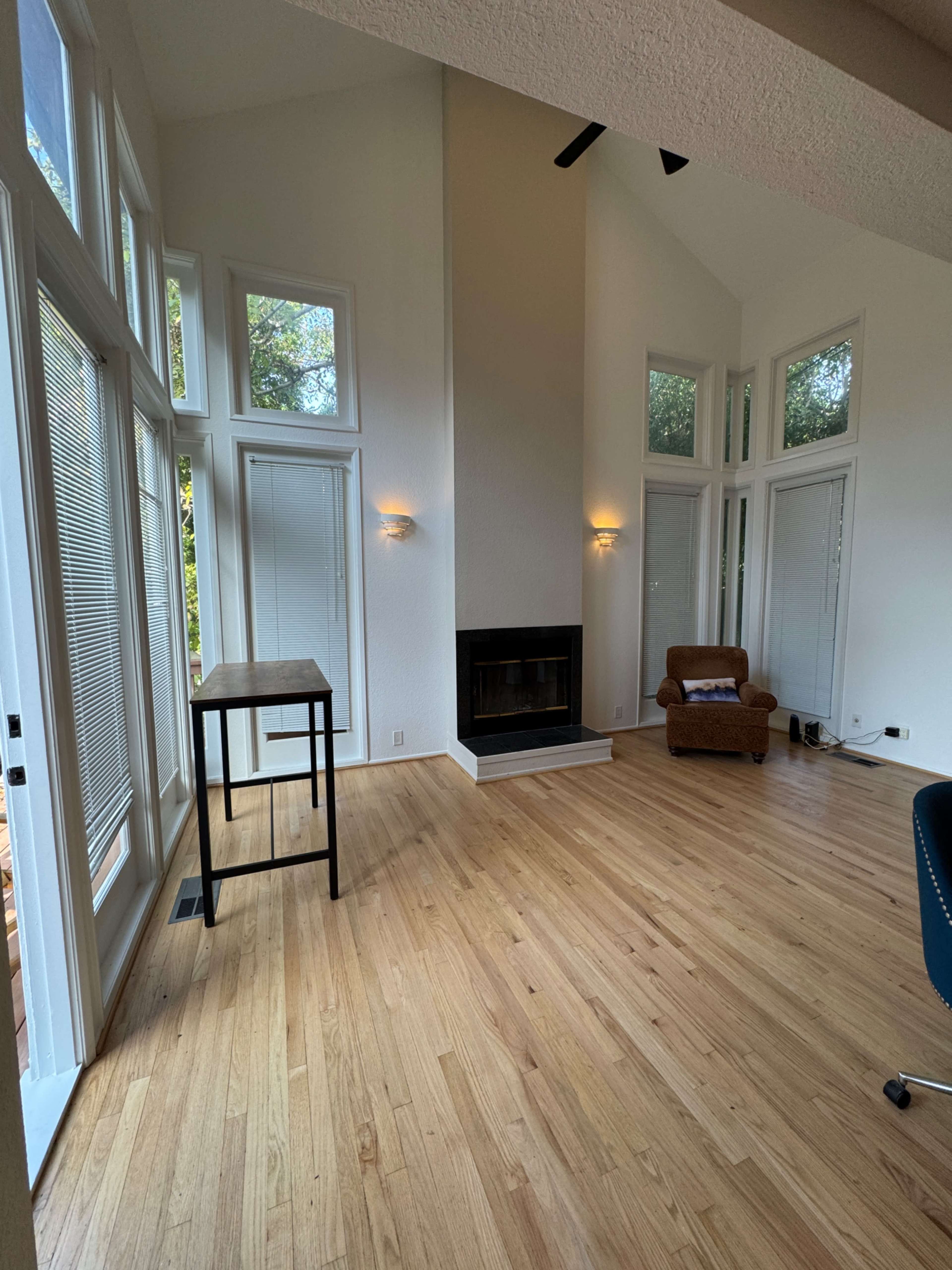 A spacious room features large windows, a central fireplace, and a wooden floor, with minimal furniture present.