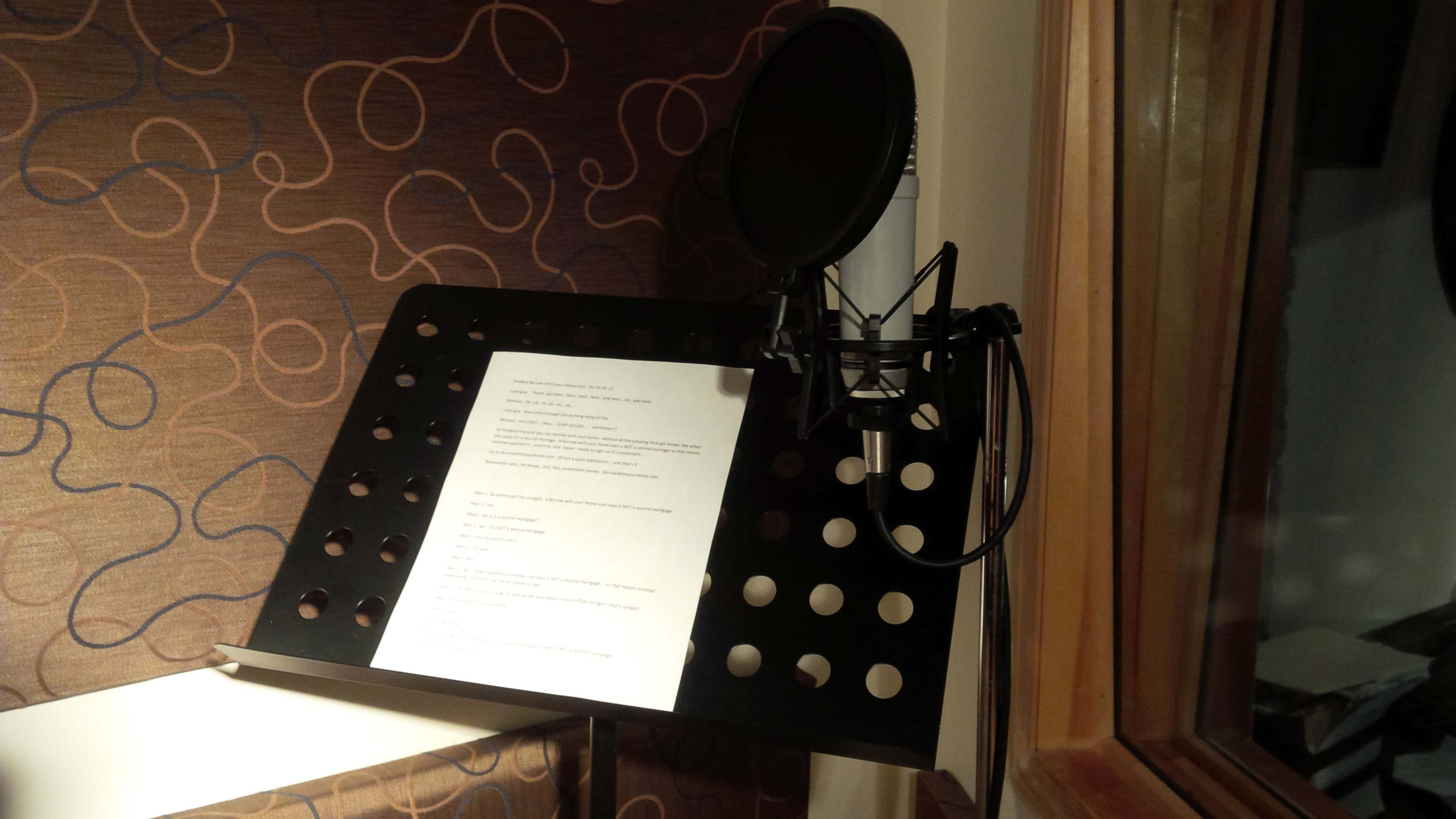 A microphone is positioned next to a music stand holding a sheet of printed text in a recording studio.
