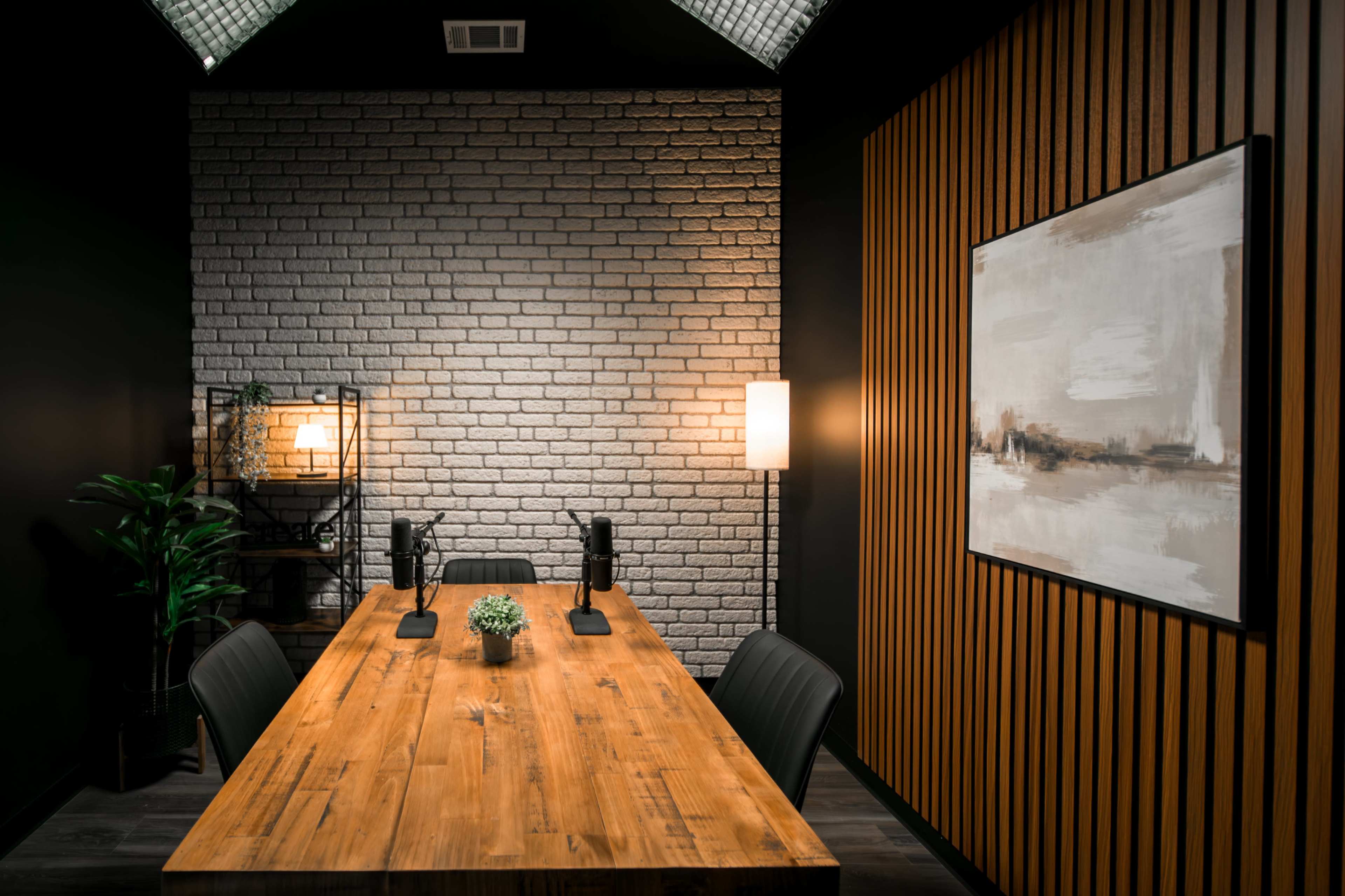 A modern conference room features a wooden table with two microphones, surrounded by black chairs, and walls of brick and wooden paneling.