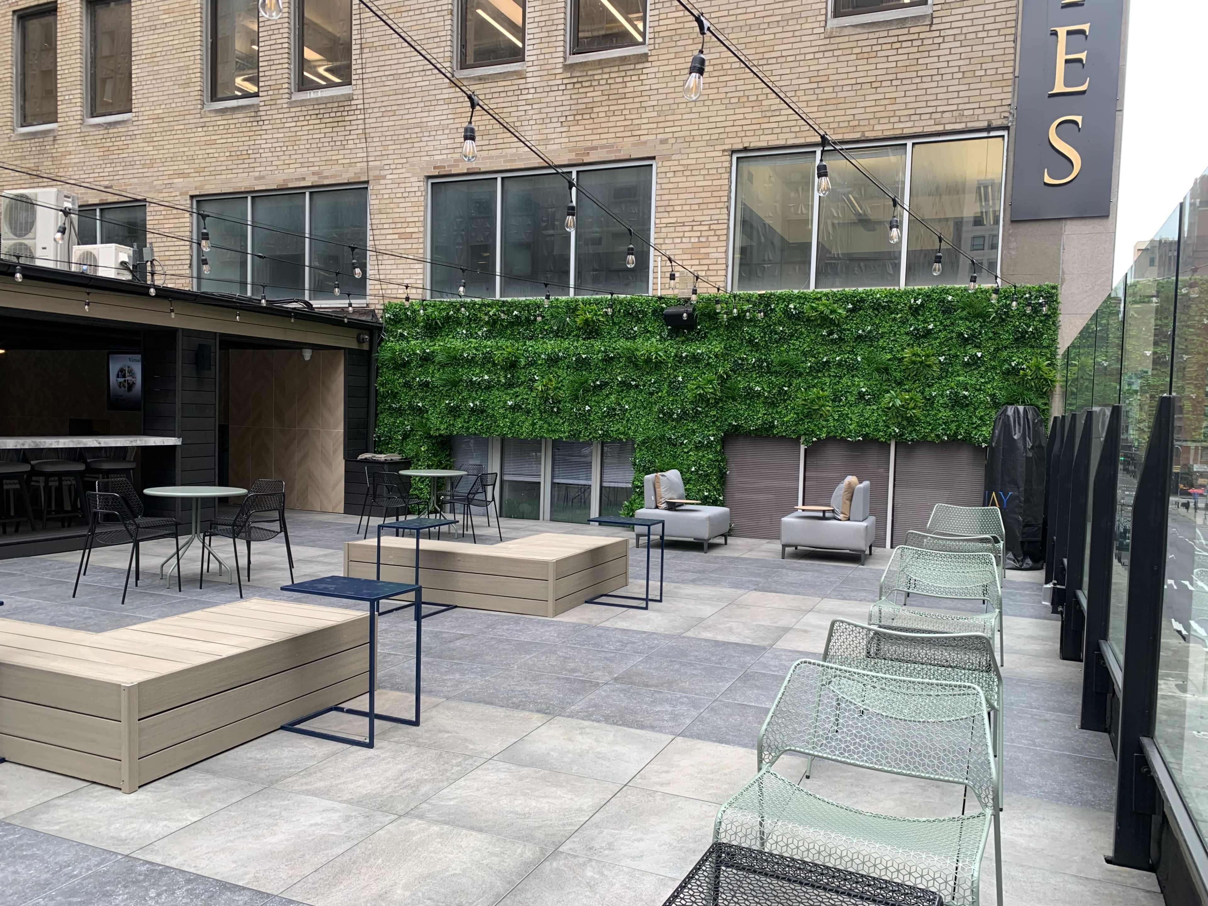 The image shows a modern outdoor patio area with green wall decor, seating arrangements, and clear overhead lighting.