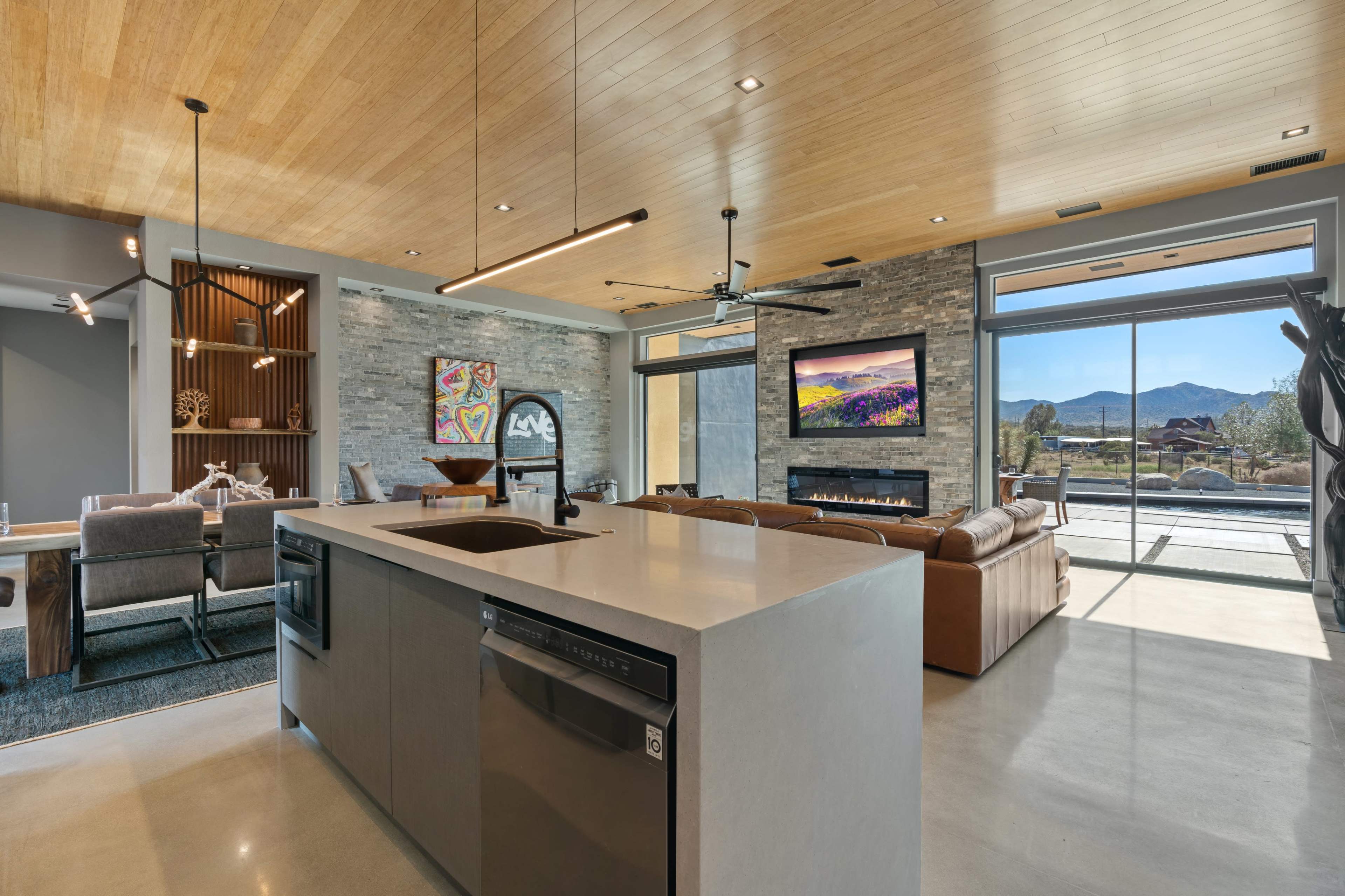A modern open-concept living space features a sleek kitchen island, a cozy seating area, and large windows that showcase a mountain view.