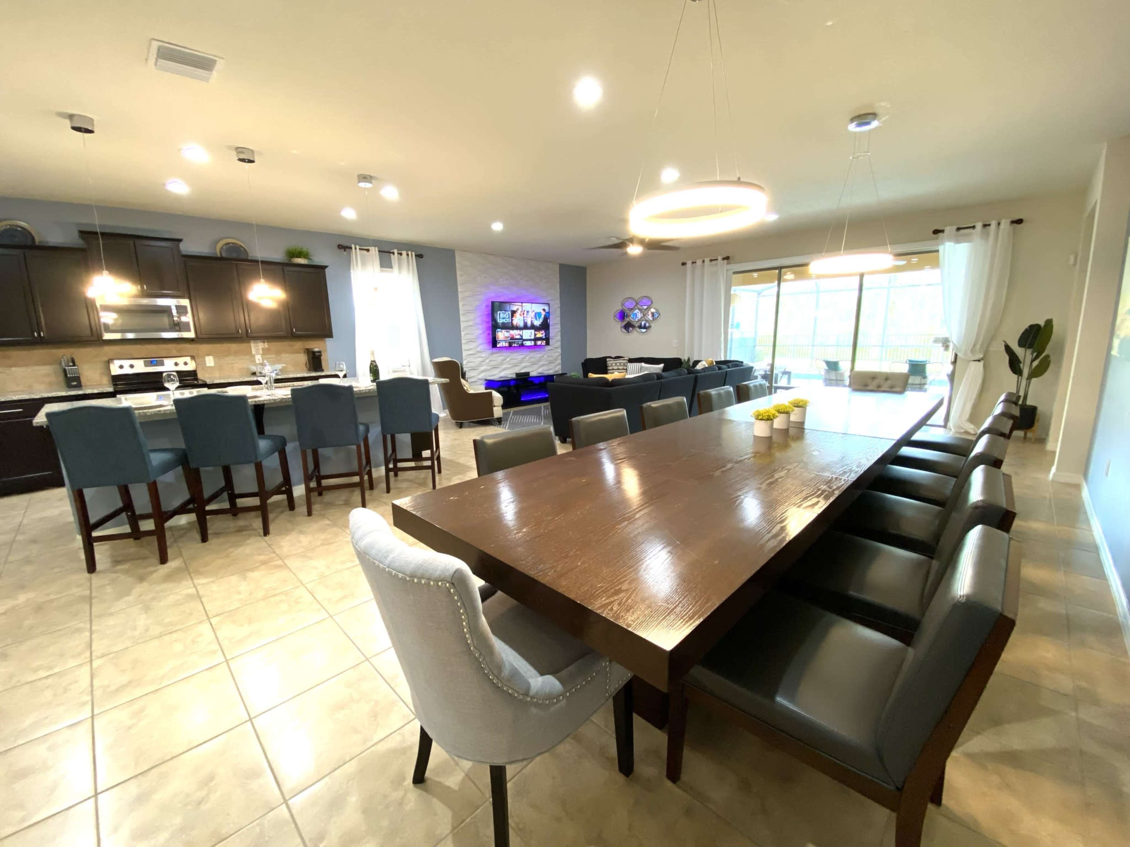 A modern open-concept kitchen and dining area with a large table, eight chairs, and a television mounted on the wall.