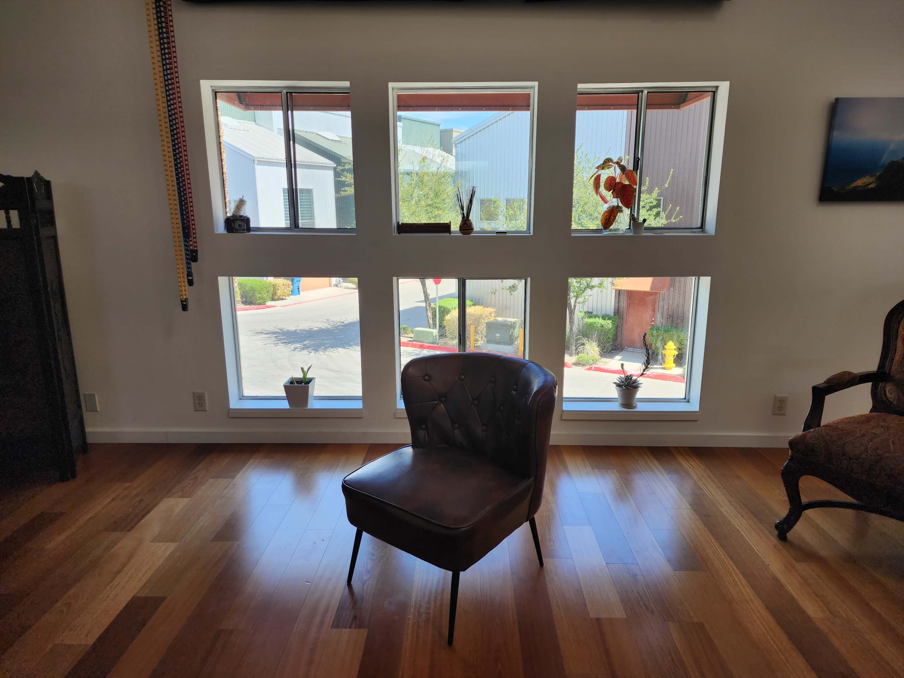 A single leather chair positioned in the center of a room with large windows on one wall displaying a view of an outdoor area.