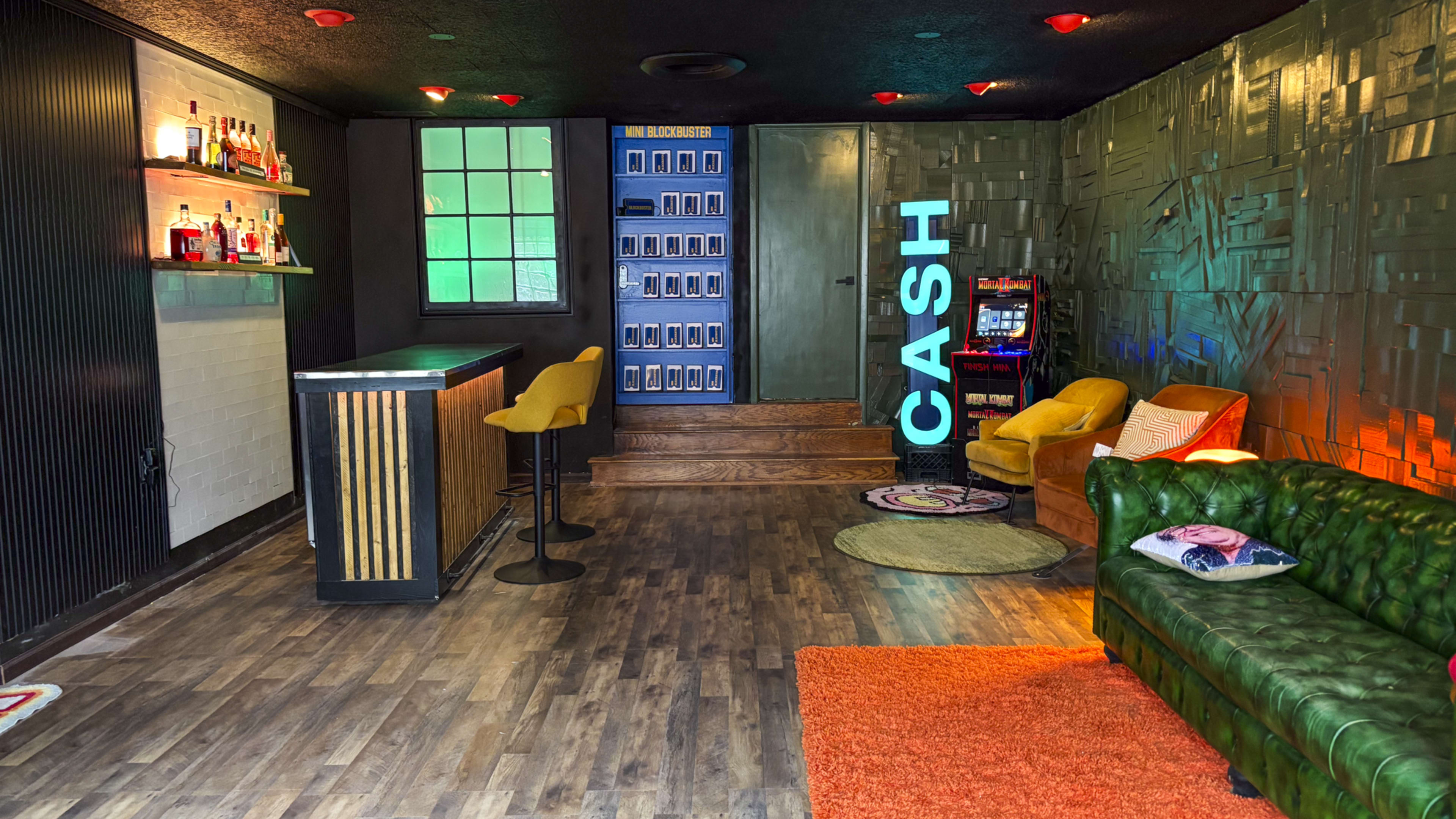 The image shows a lounge area with a bar, seating, and a colorful décor, including a "CASH" sign and a gaming machine.