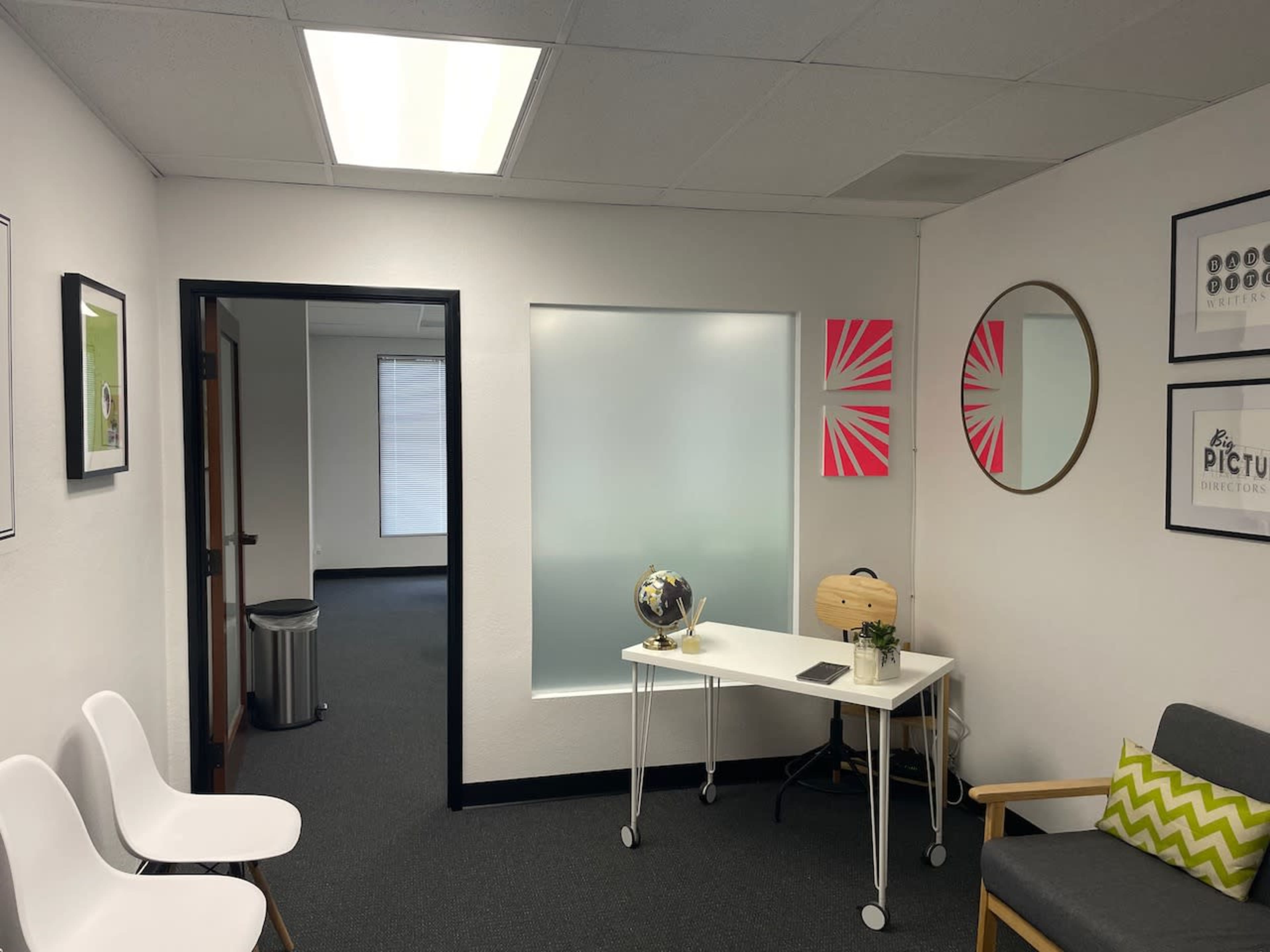 A modern office waiting area with white walls, a desk, a globe, two chairs, and bright wall decorations.