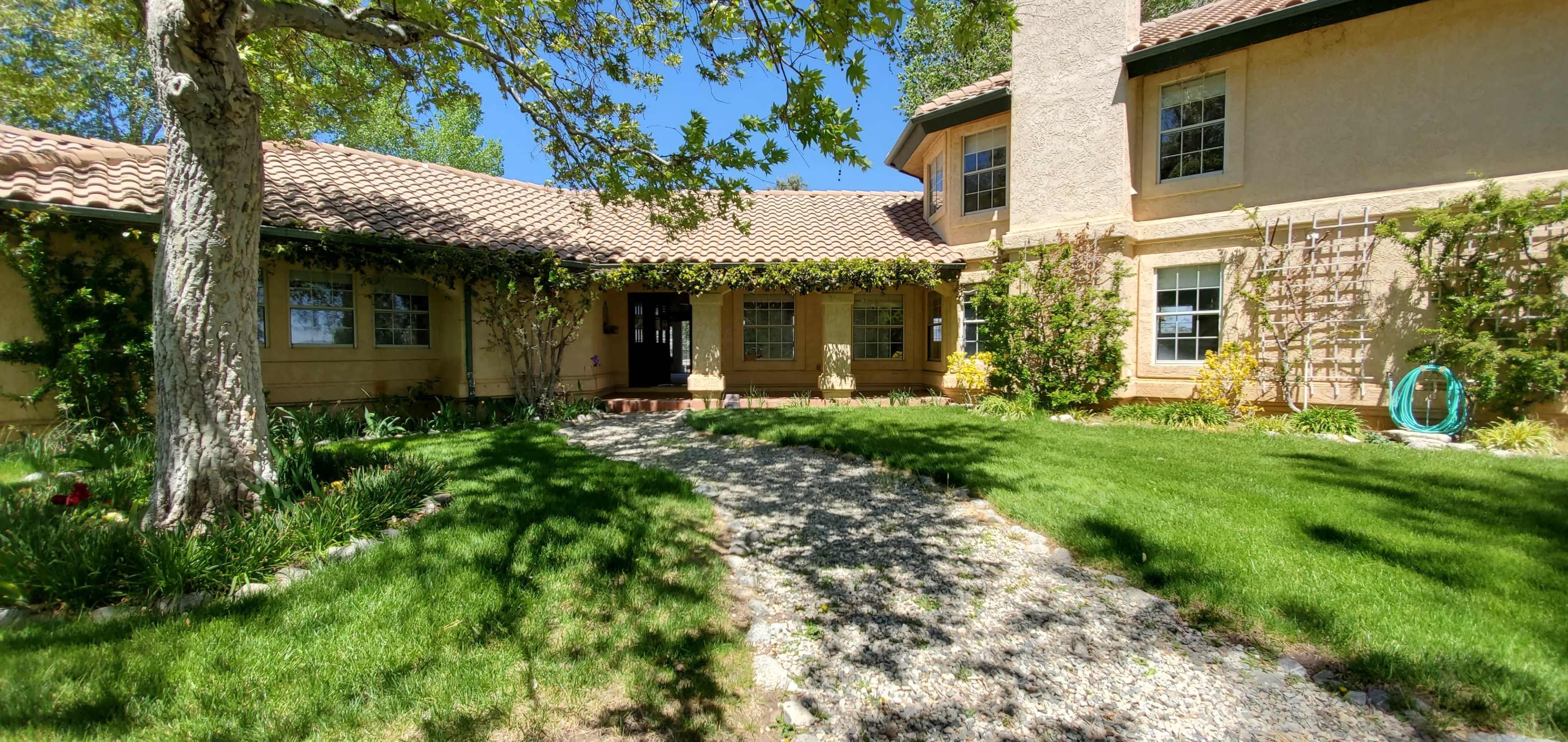 A large, two-story house with a tiled roof and front porch is surrounded by green grass and trees.