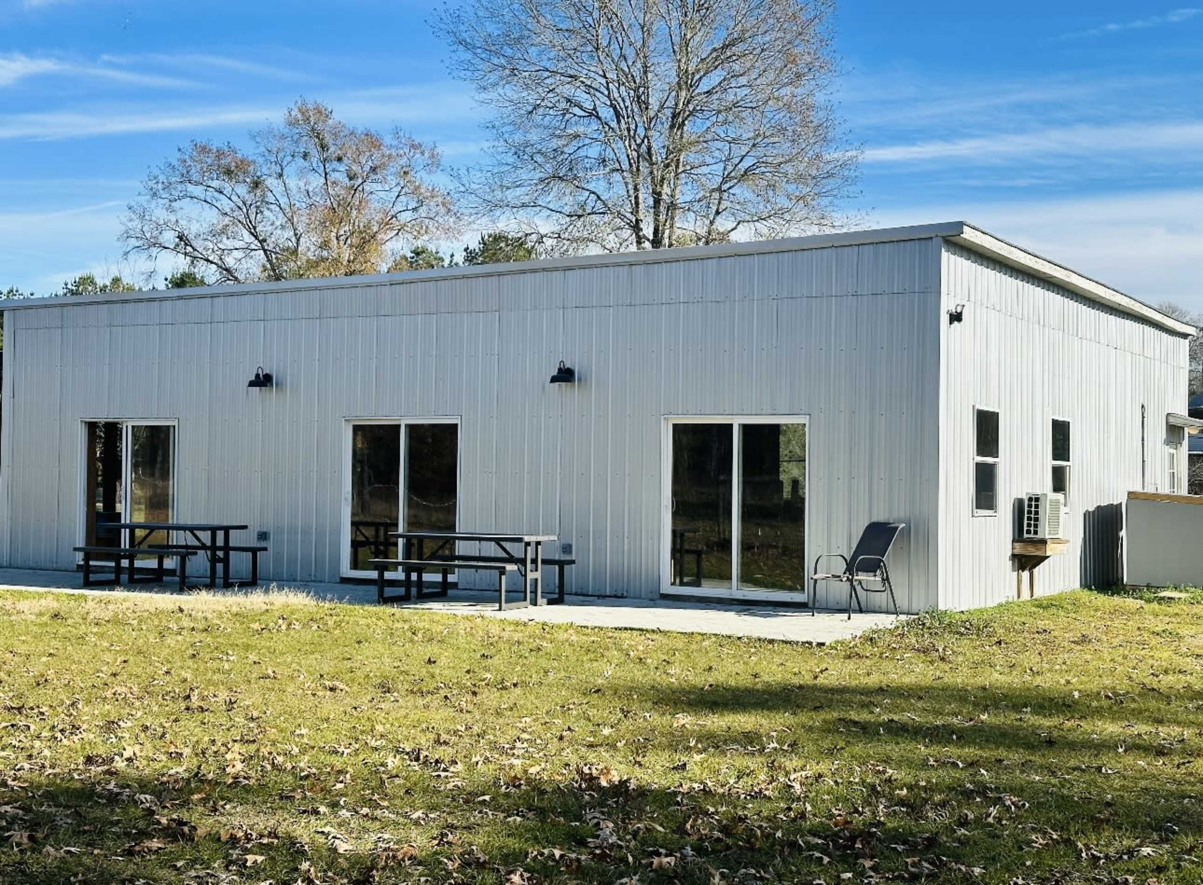 A single-story metal building with large windows and outdoor seating areas is situated on a grassy lot.