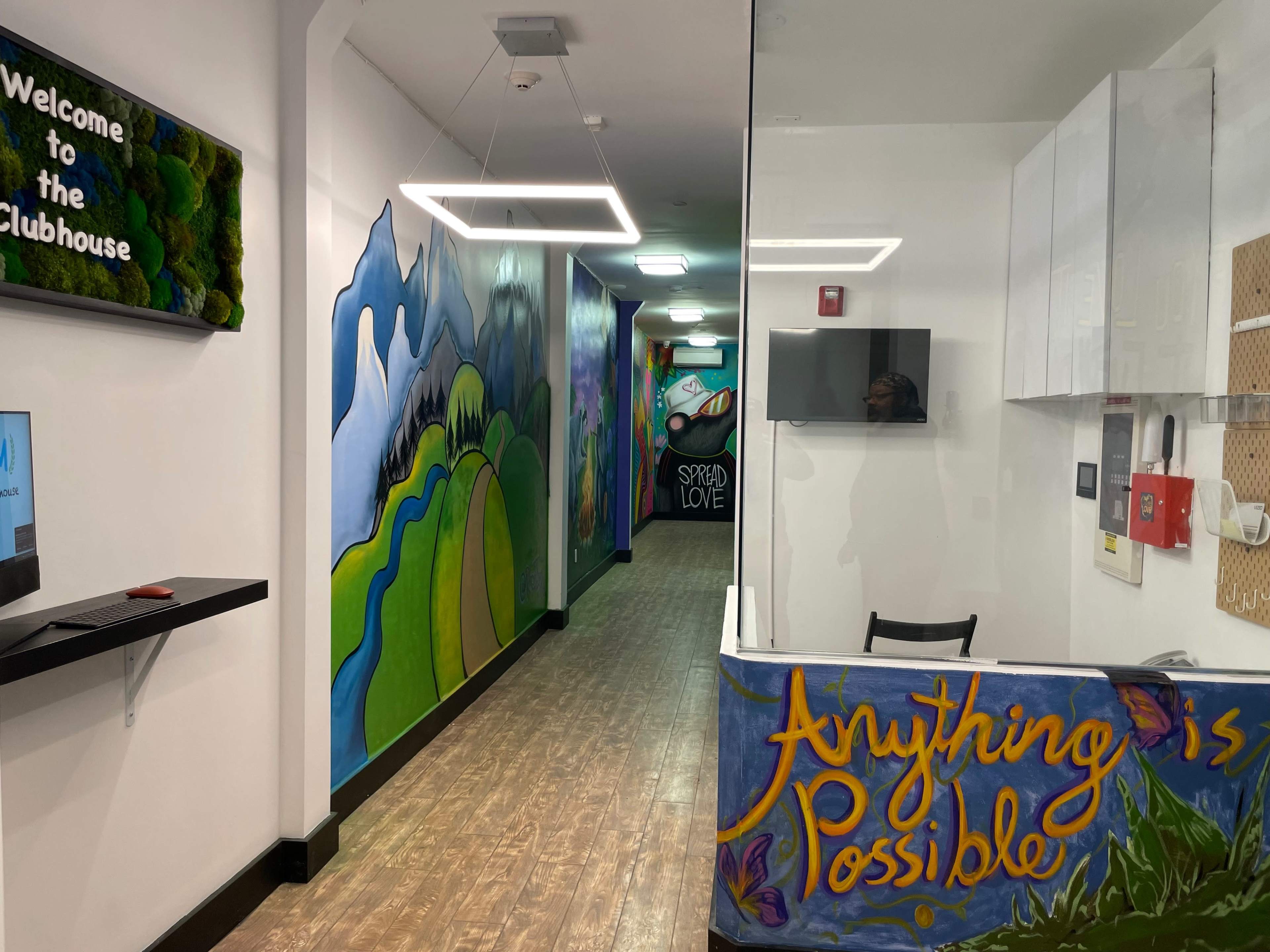 The image shows a brightly painted interior corridor with colorful murals on the walls, leading to different rooms within a clubhouse.