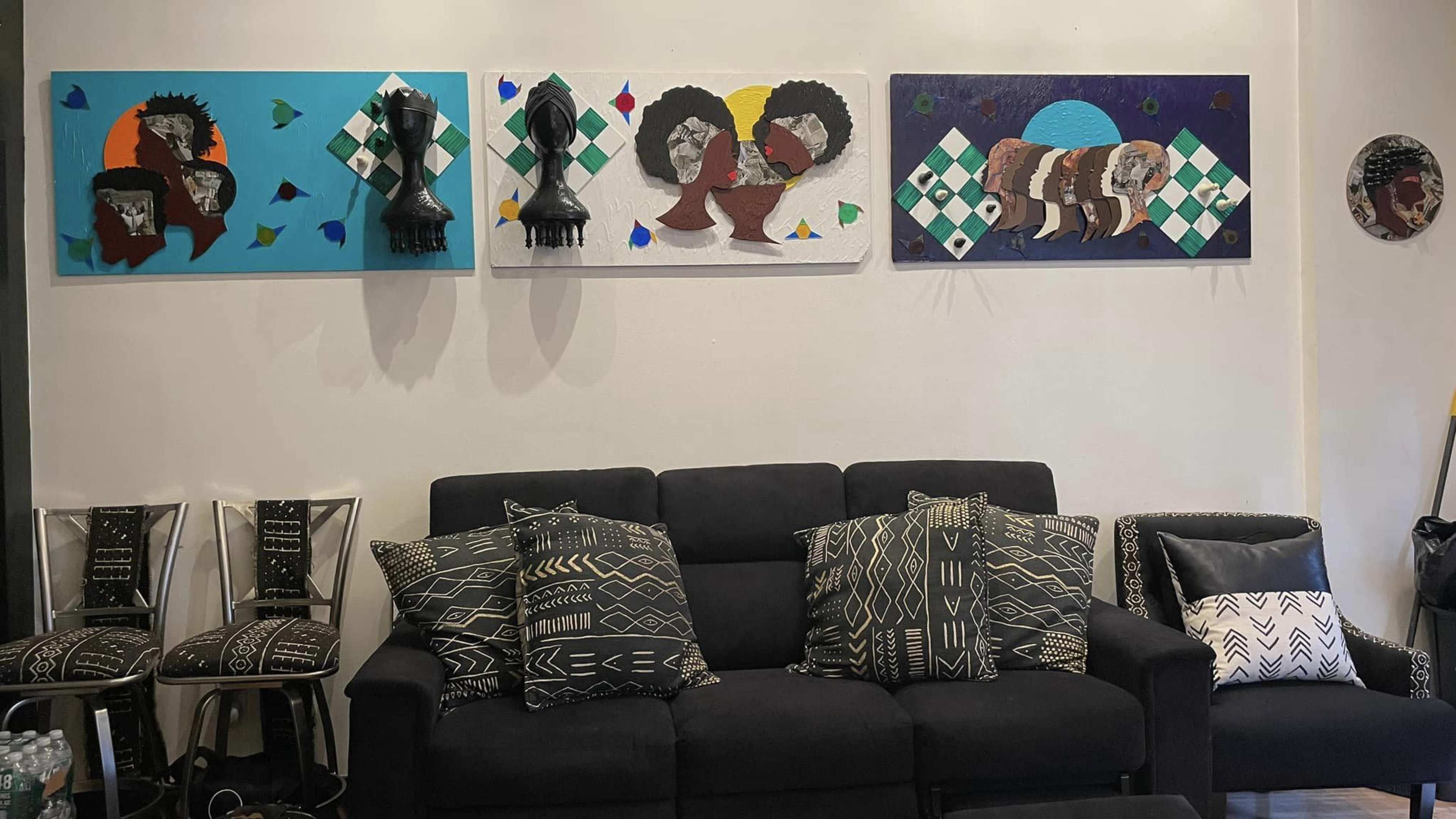 A modern living room with a black couch and patterned cushions, adorned with colorful abstract paintings on the wall and black-and-white patterned chairs nearby.