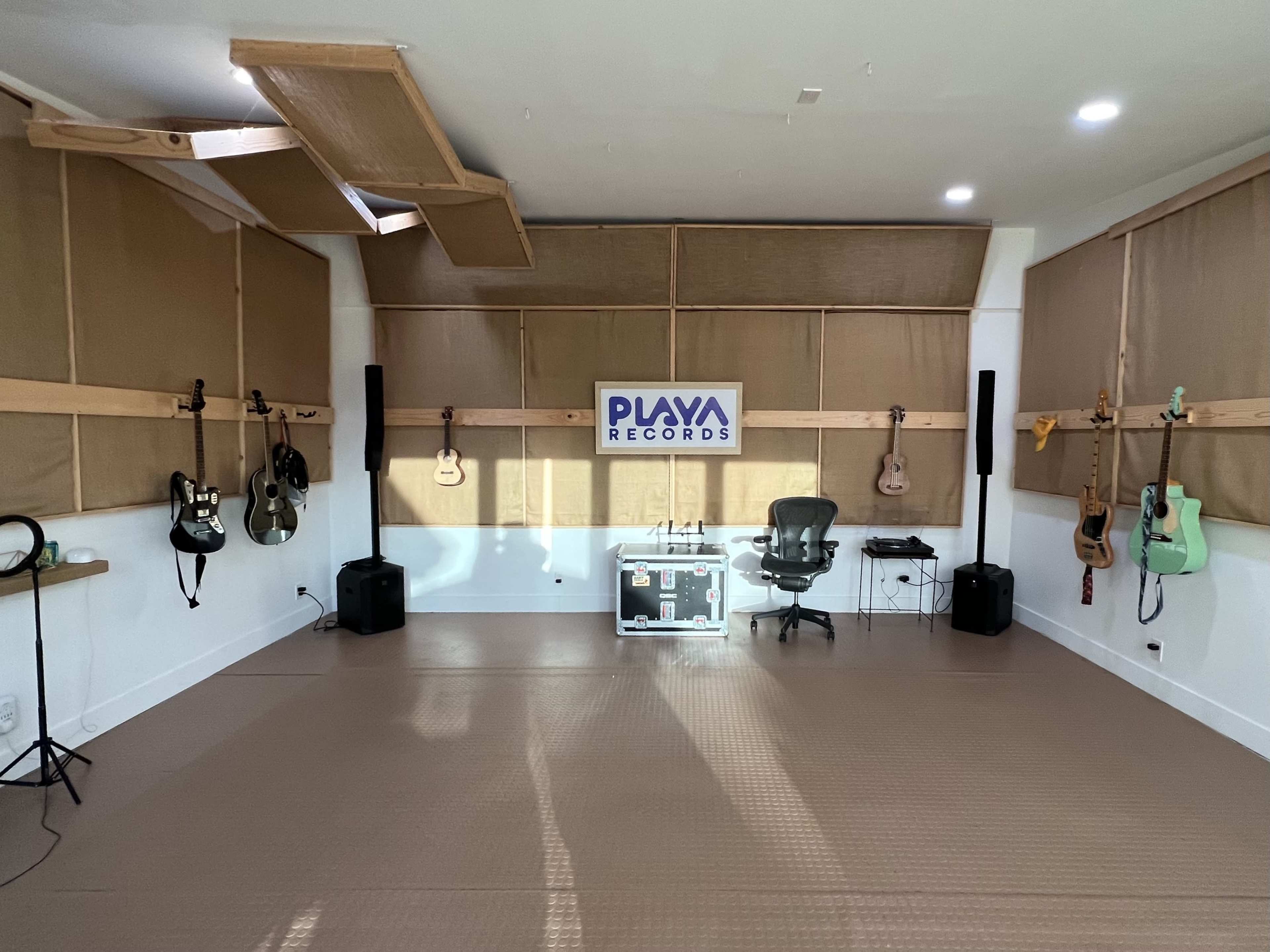 The image shows a music recording studio featuring guitars on the walls, soundproofing panels, a central workstation with a chair, and a 'PLAYA RECORDS' sign.