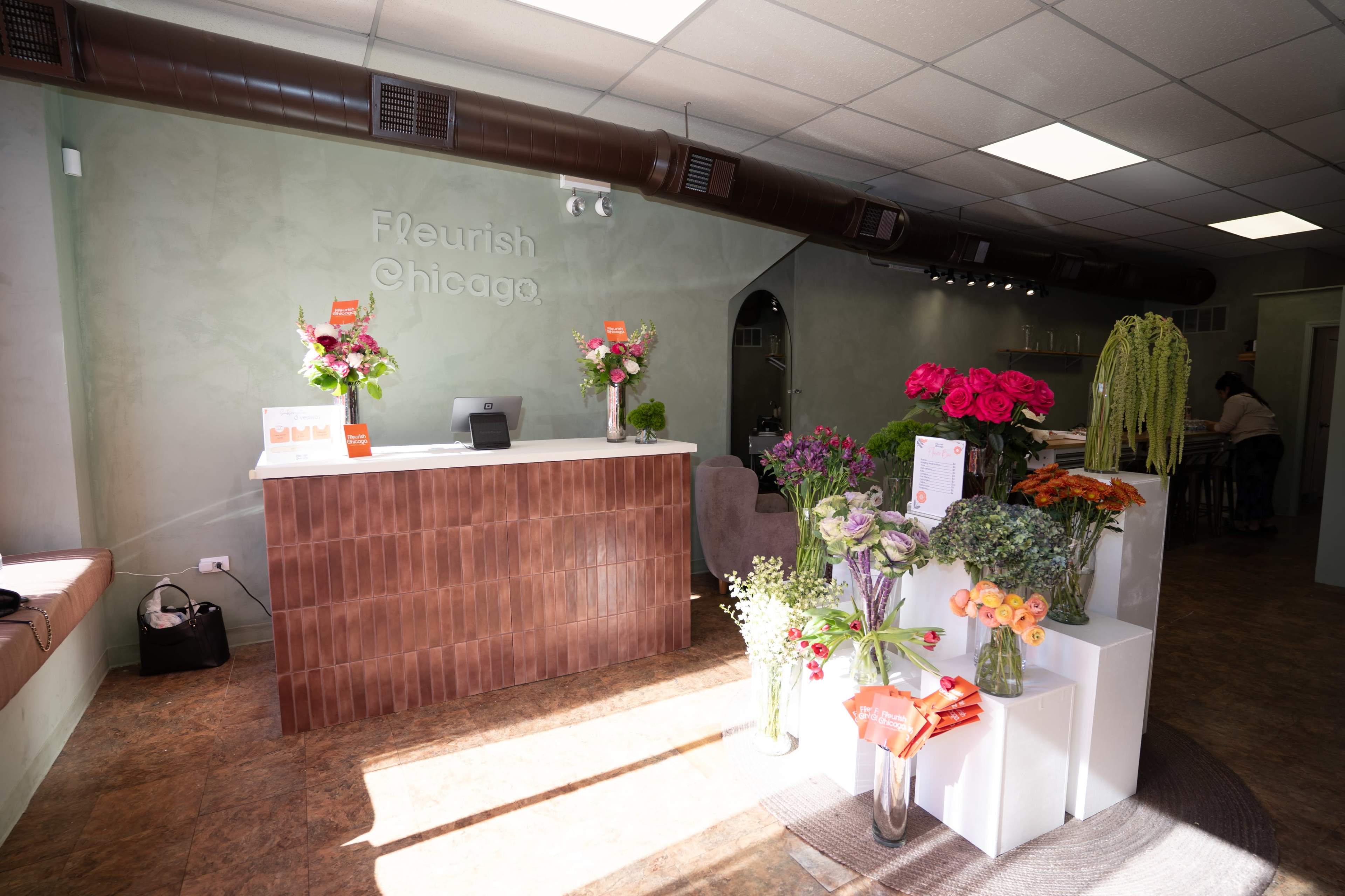 The image shows a florist shop interior with a reception counter, flower arrangements in display stands, and a modern decor style.