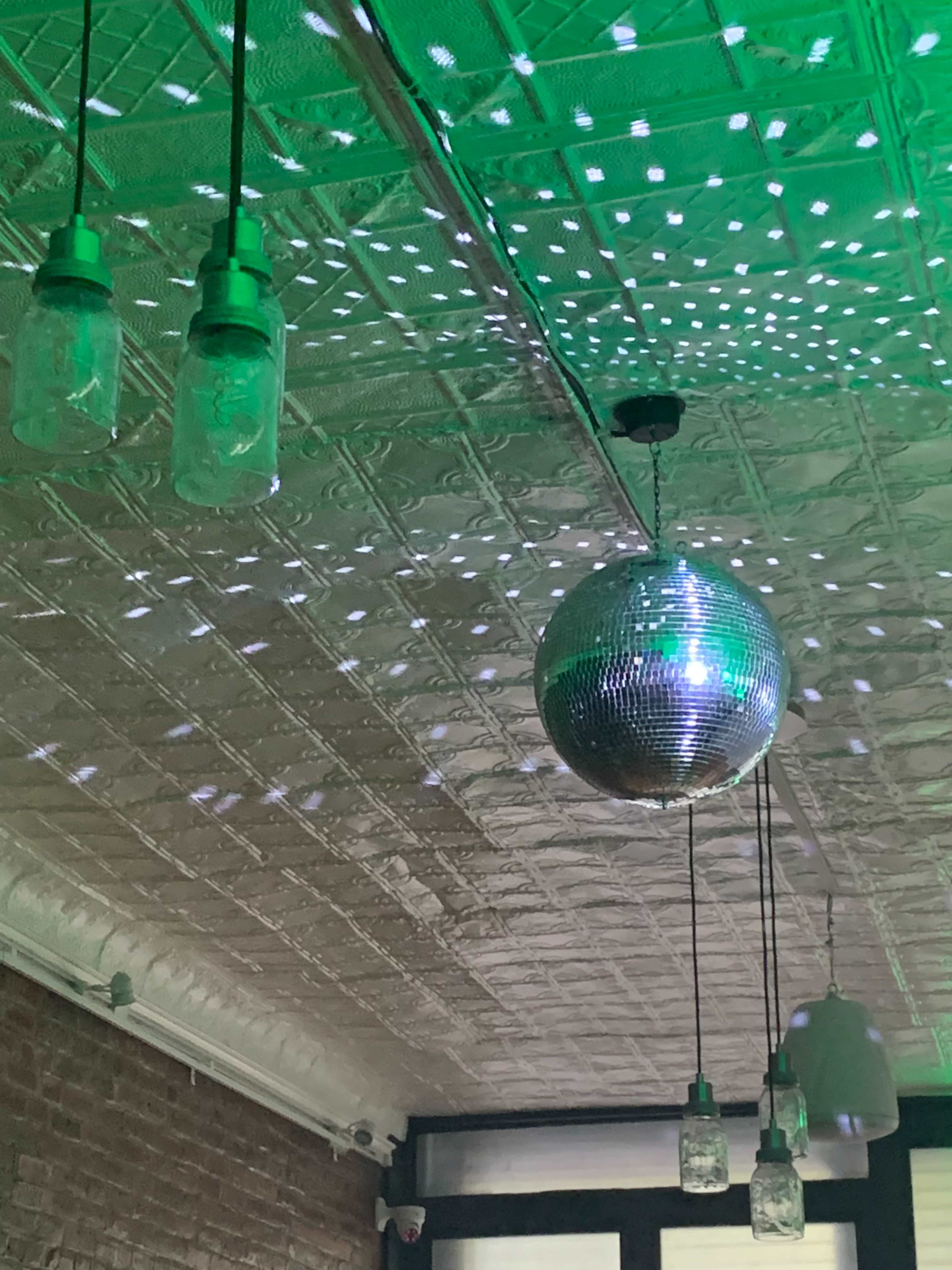 A ceiling with a disco ball and three hanging glass light fixtures, reflecting light across the surface.