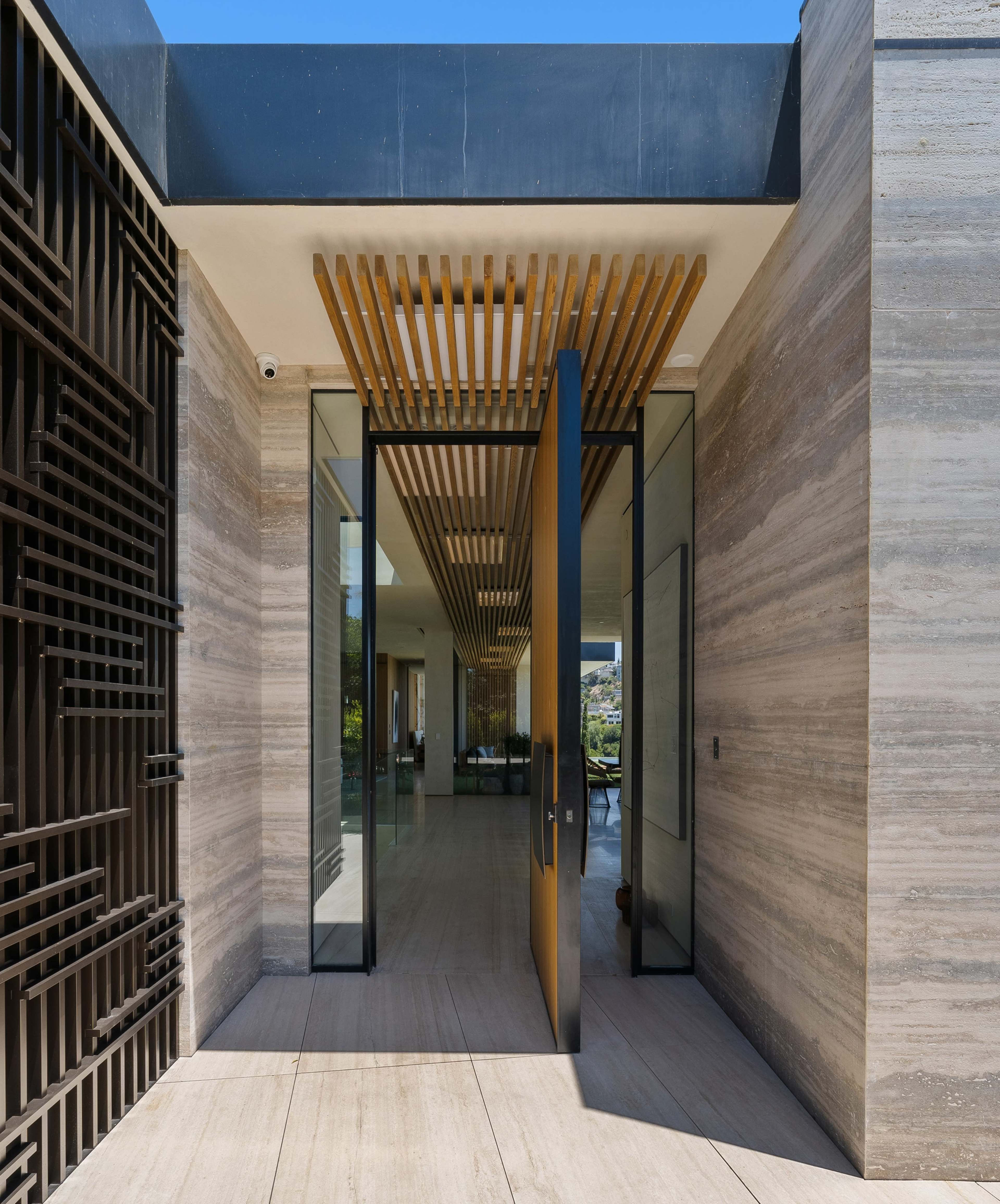 A modern entrance with large glass doors and a wood slat ceiling, opening to a spacious interior.