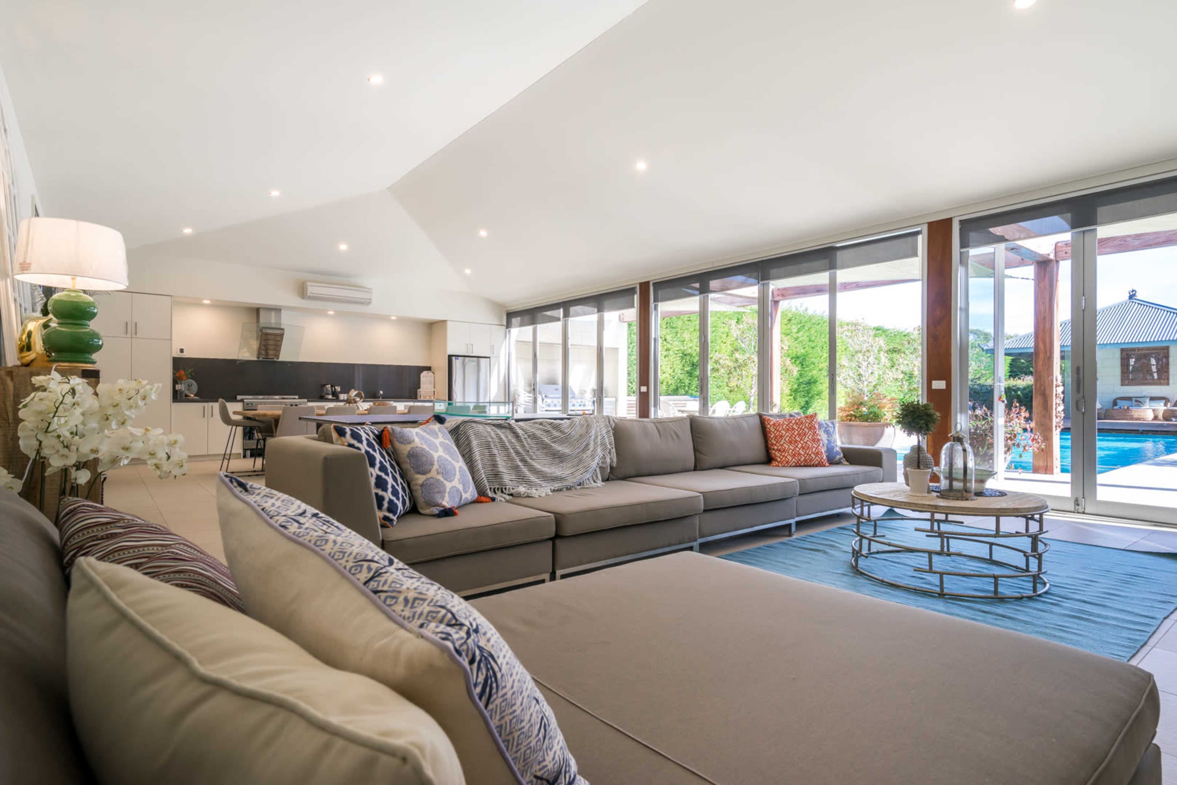 A spacious modern living room with a large sectional sofa, a coffee table, and sliding glass doors leading to an outdoor pool area.