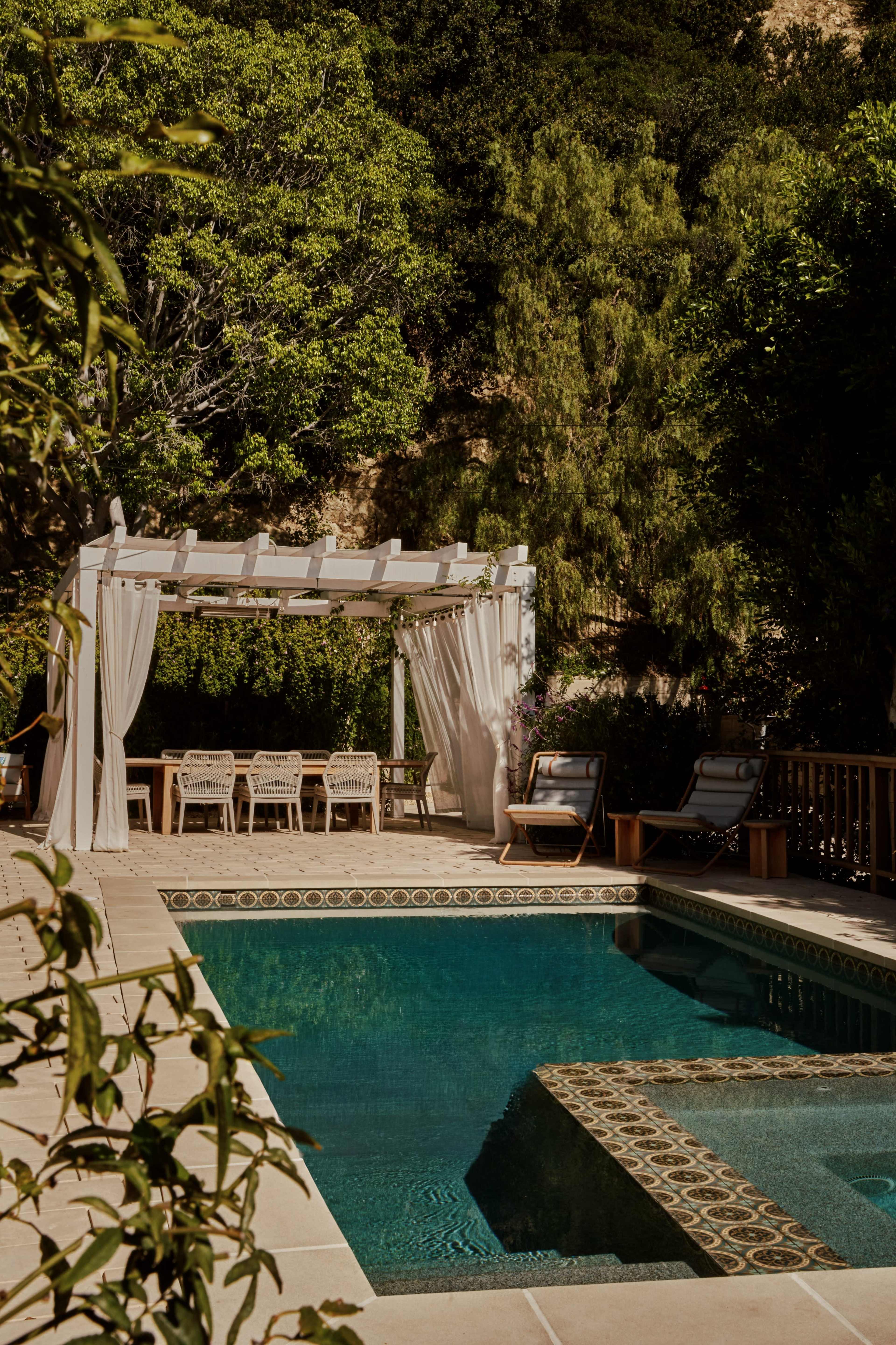 The image shows a backyard pool area with a pergola, lounge chairs, and a decorative tile border around the pool.