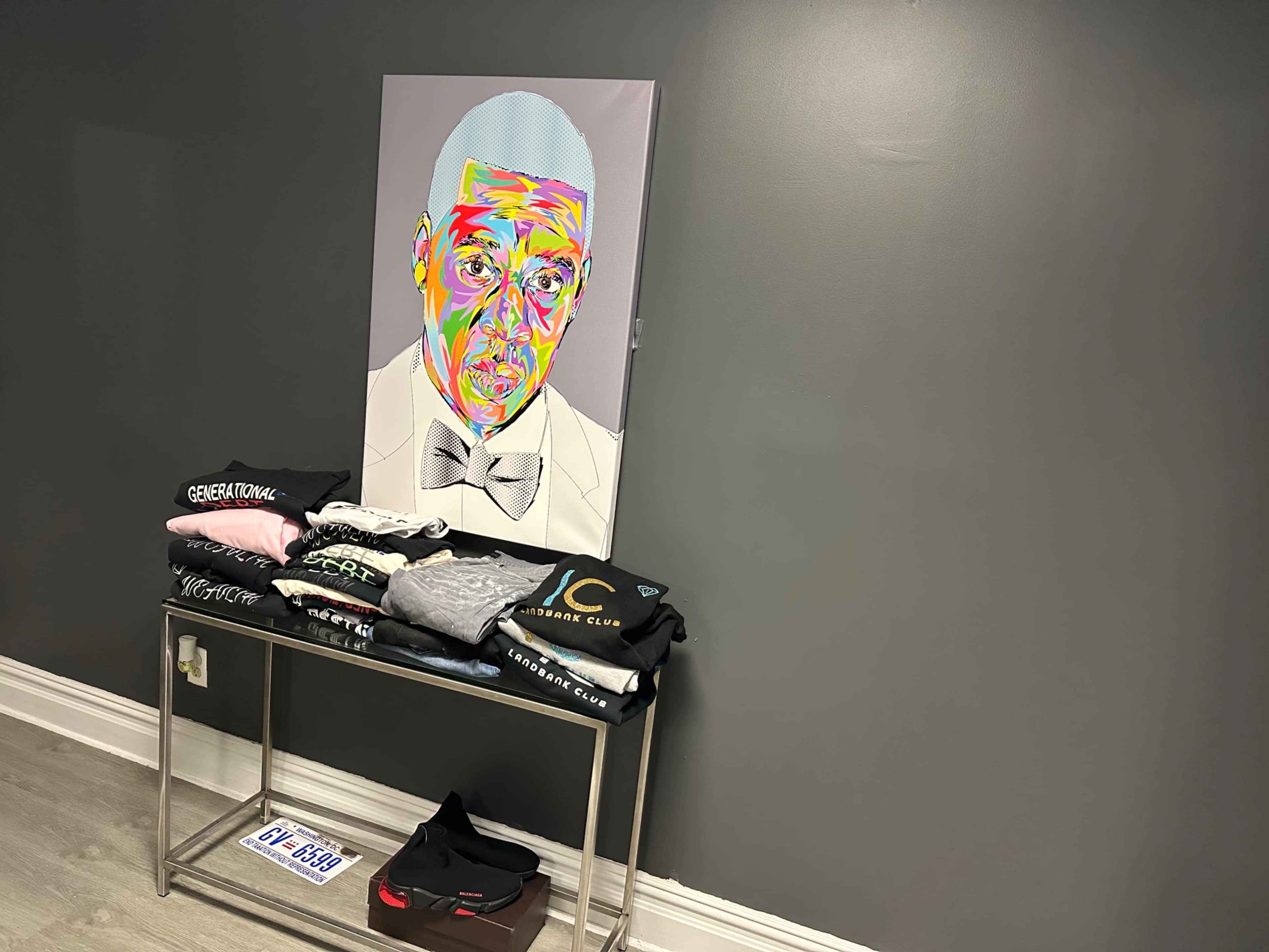 A colorful portrait of a man is displayed on a wall beside a table stacked with neatly folded T-shirts.