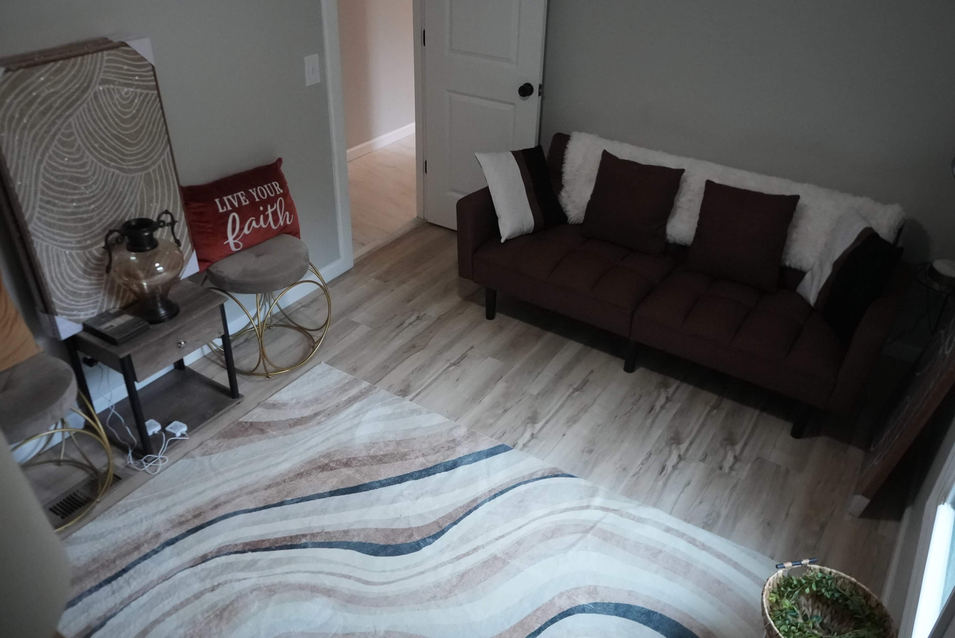 The image shows a cozy living room with a brown sofa, two round side tables, and a patterned area rug on a light-colored wooden floor.