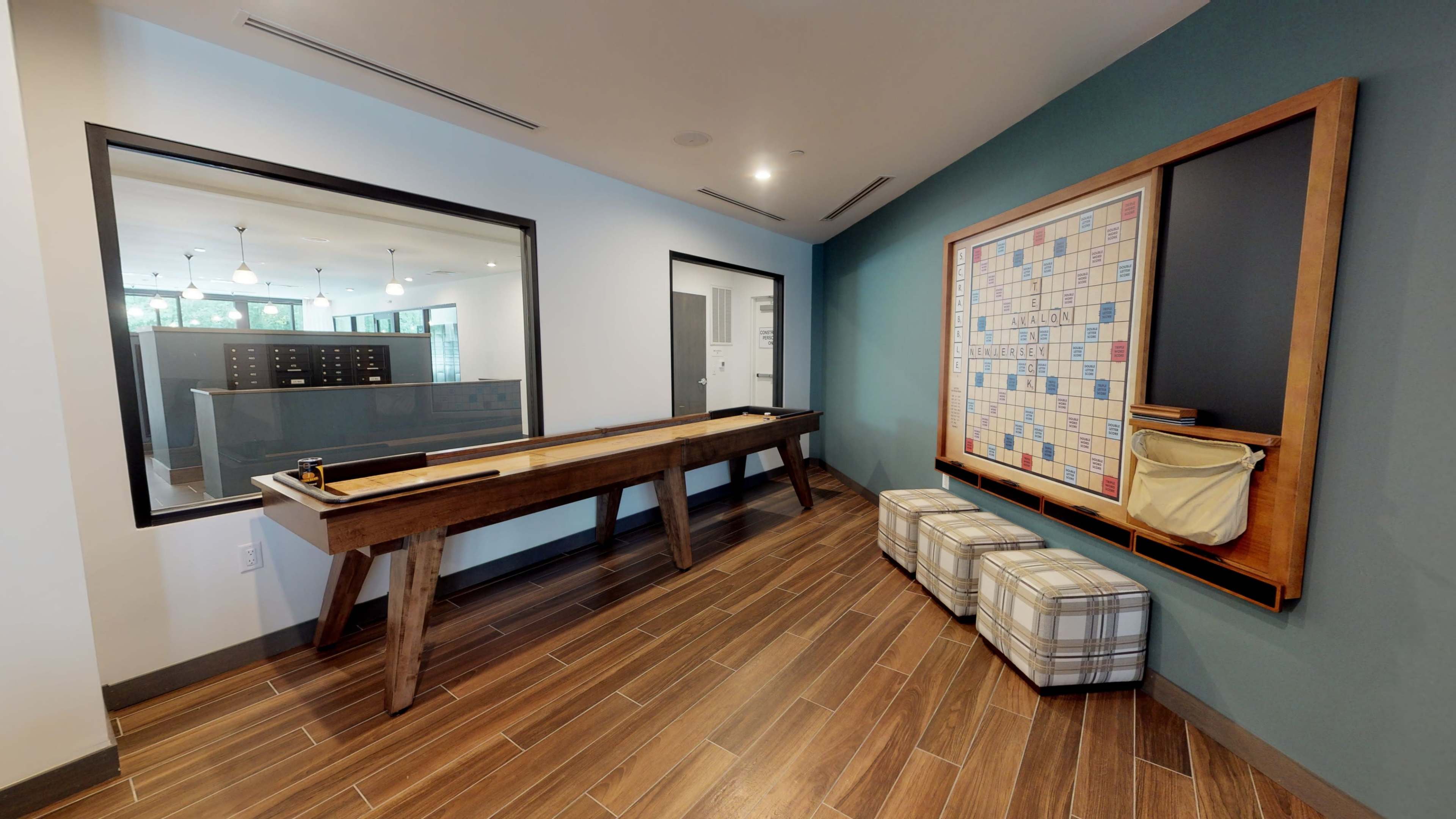 A recreational area featuring a shuffleboard table, a bulletin board, and two patterned ottomans against a blue accent wall.