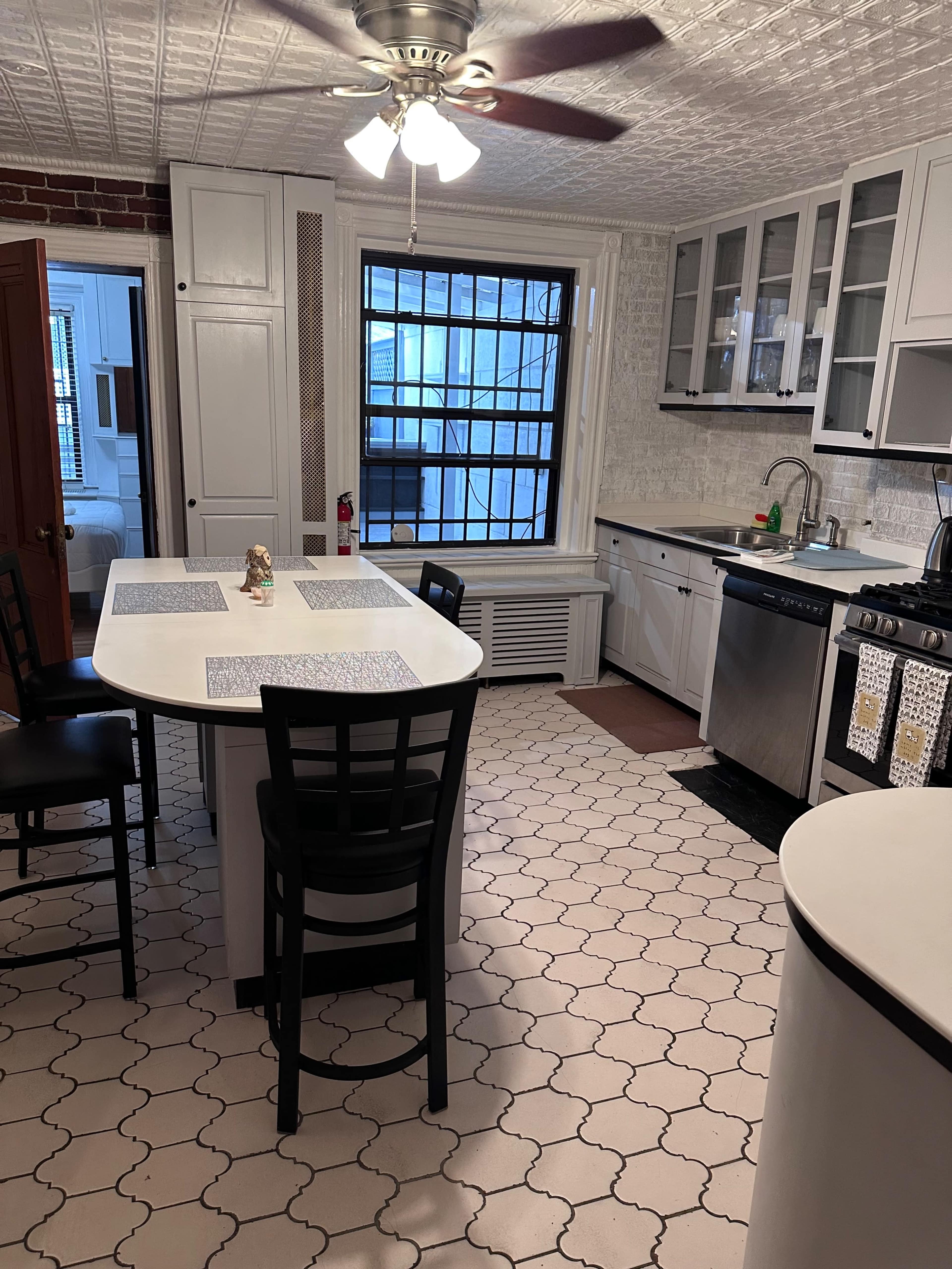 The kitchen features a central island with seating, stainless steel appliances, and tiled flooring in a geometric pattern.