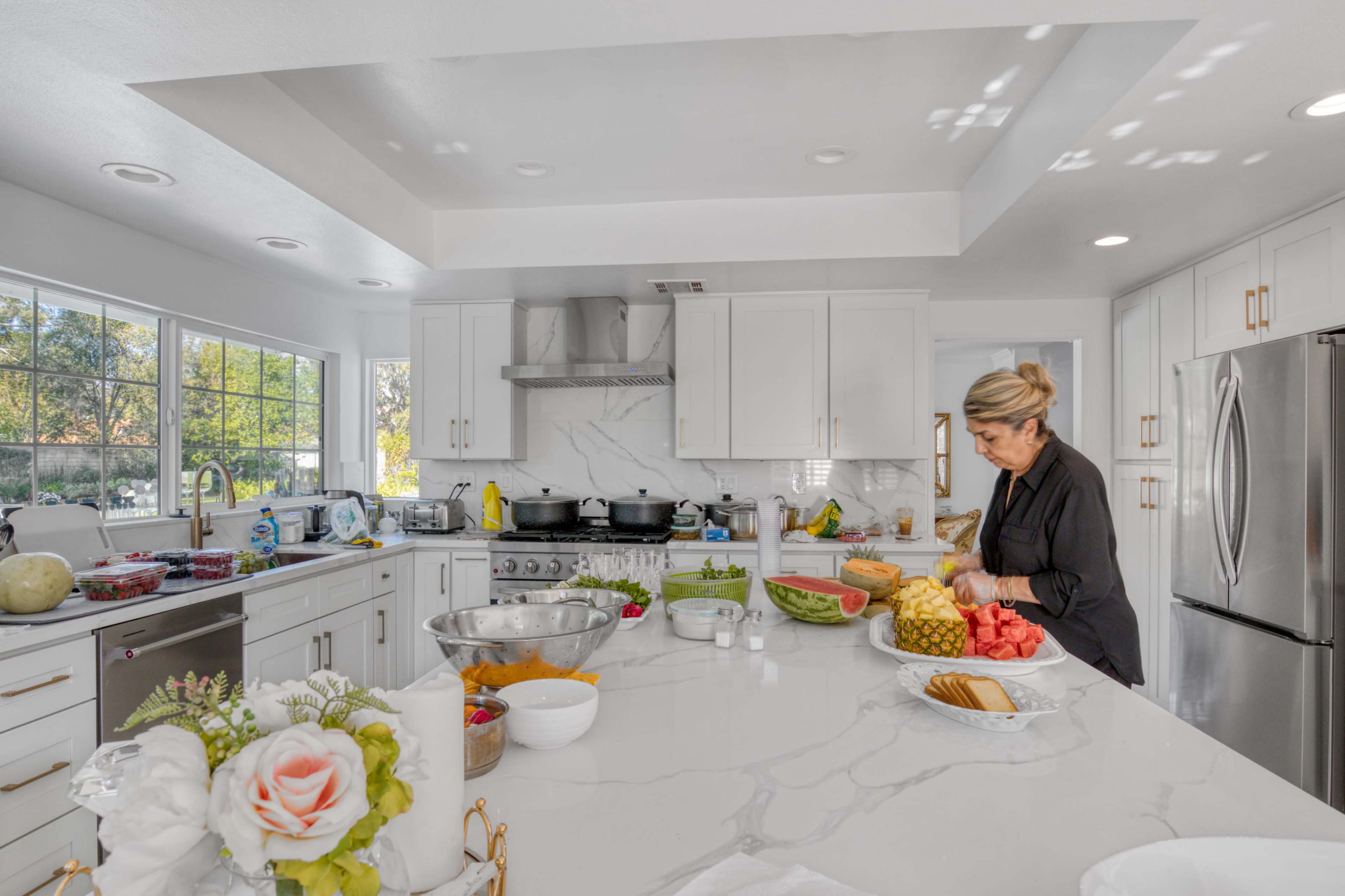 A woman prepares food in a modern kitchen with white cabinetry and a marble countertop.
