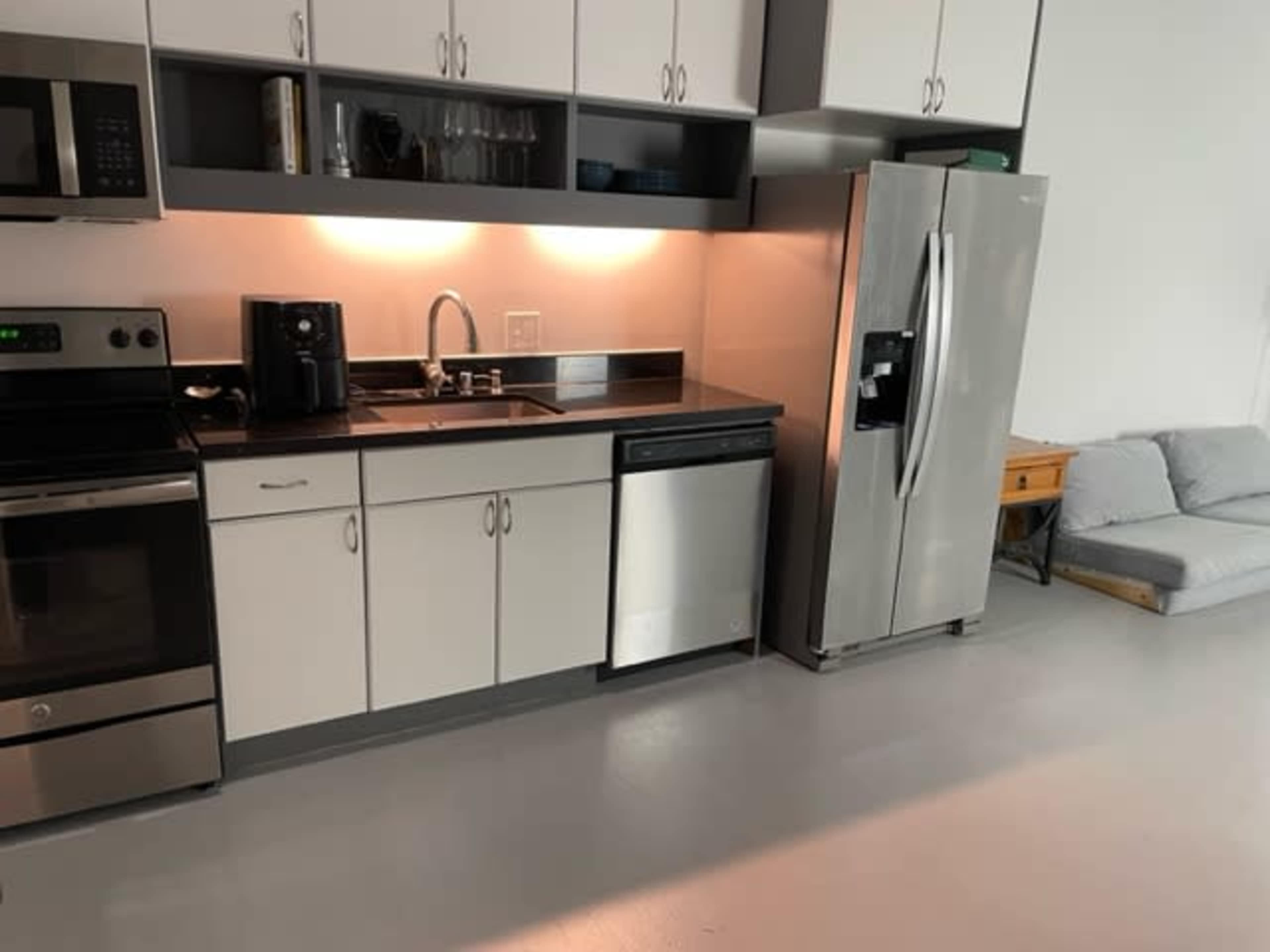 The image shows a modern kitchen with black and stainless steel appliances, including an oven, microwave, and refrigerator, with white cabinets and a sink.
