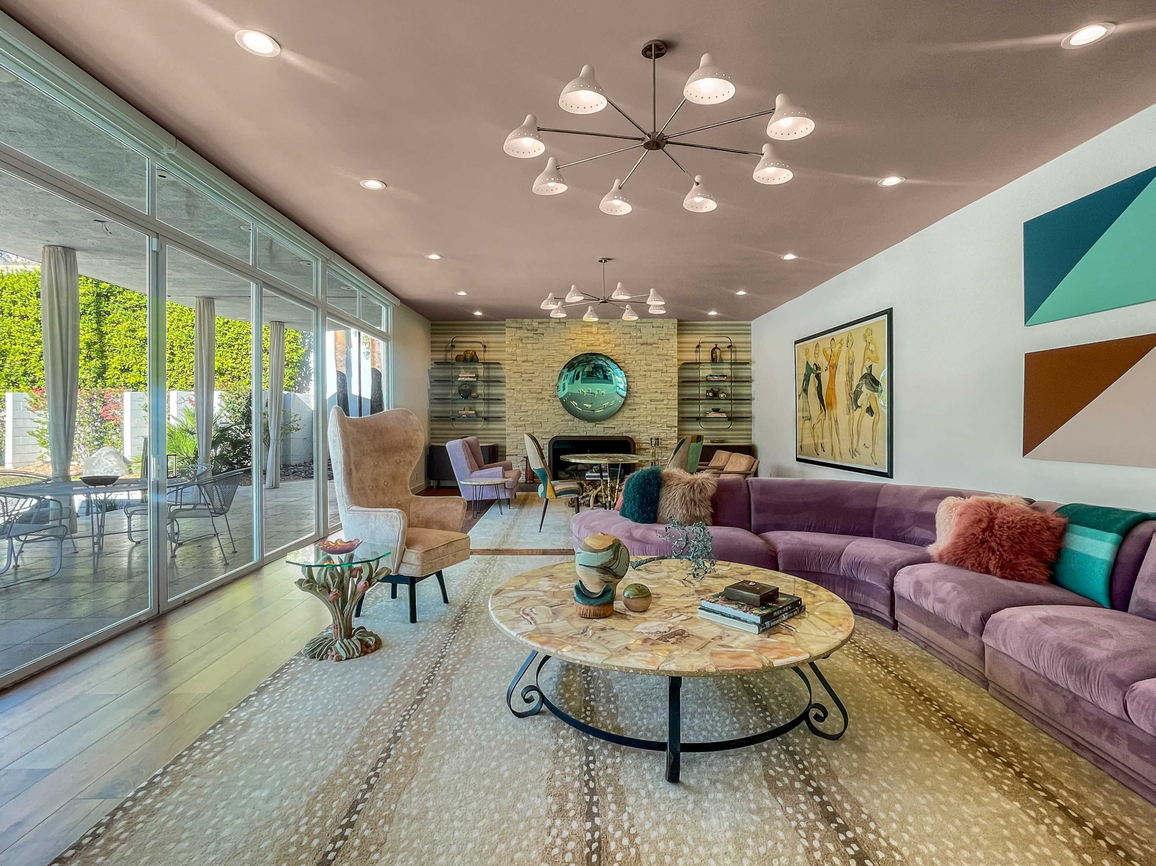 A modern living room featuring a curved purple sofa, a round coffee table, and large windows that open to an outdoor patio.