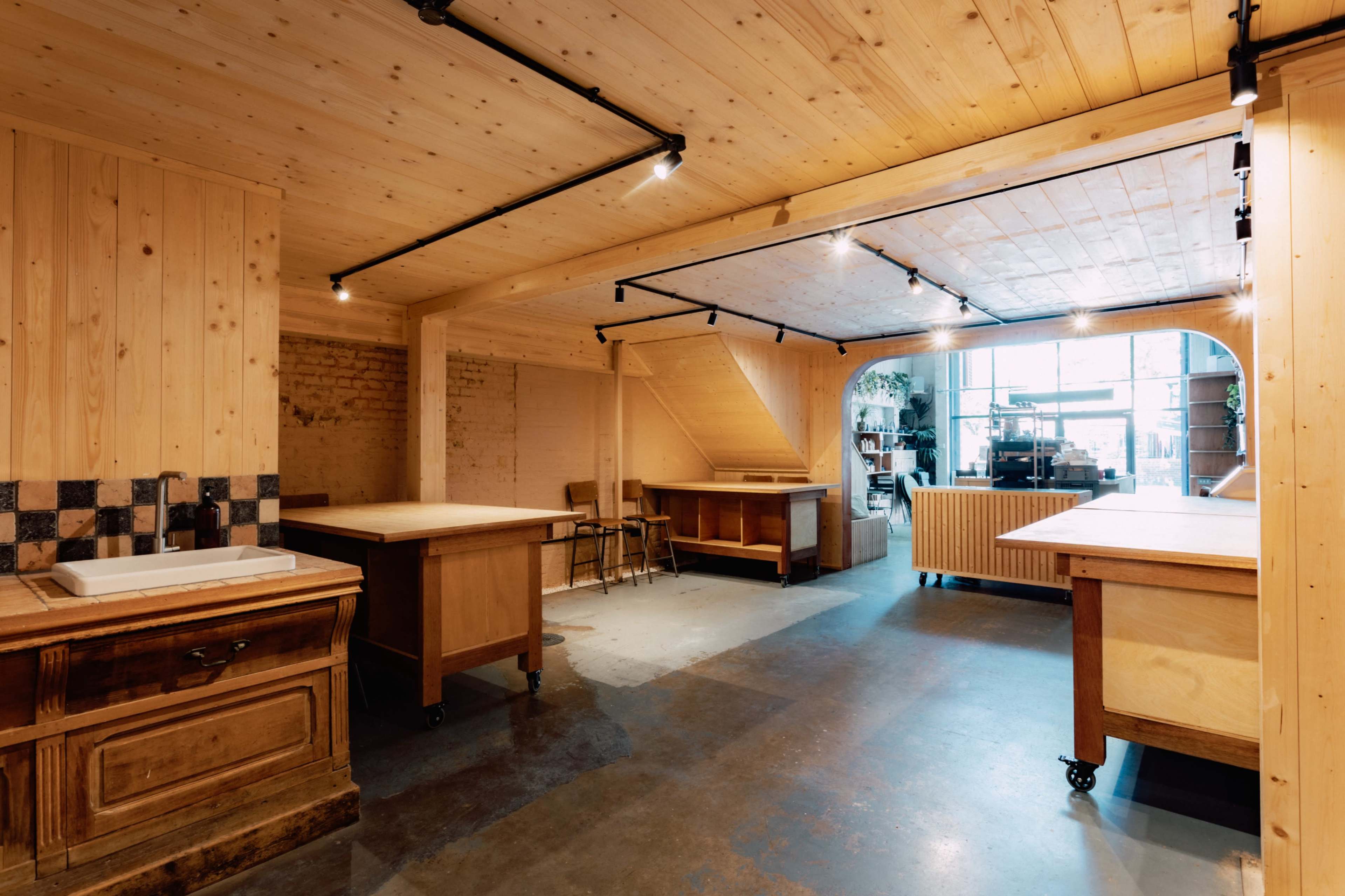 The image shows a spacious, well-lit workshop with wooden walls and various worktables arranged throughout.