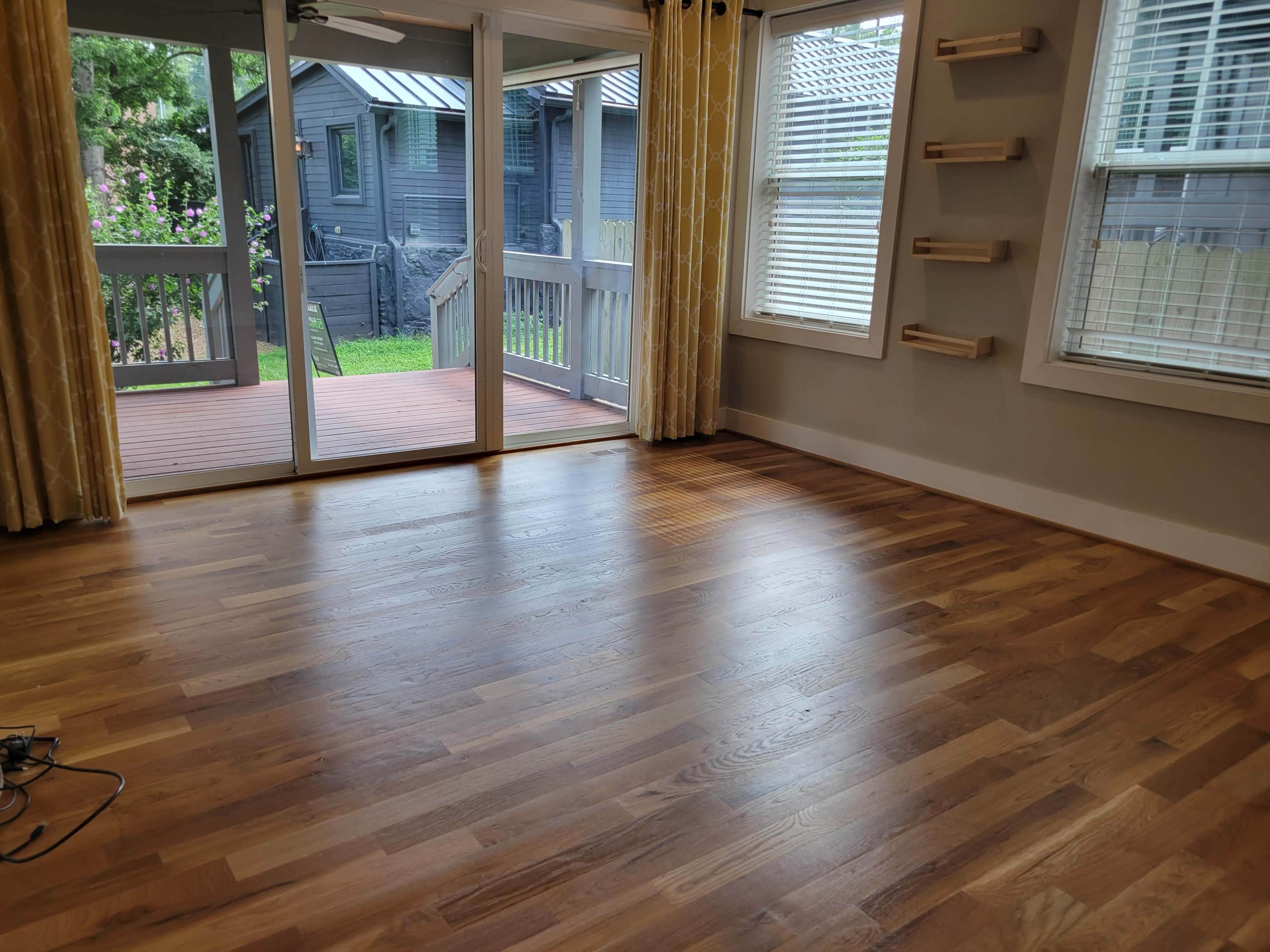 The image shows a living room with hardwood flooring, large windows, and a sliding glass door leading to a deck and backyard.