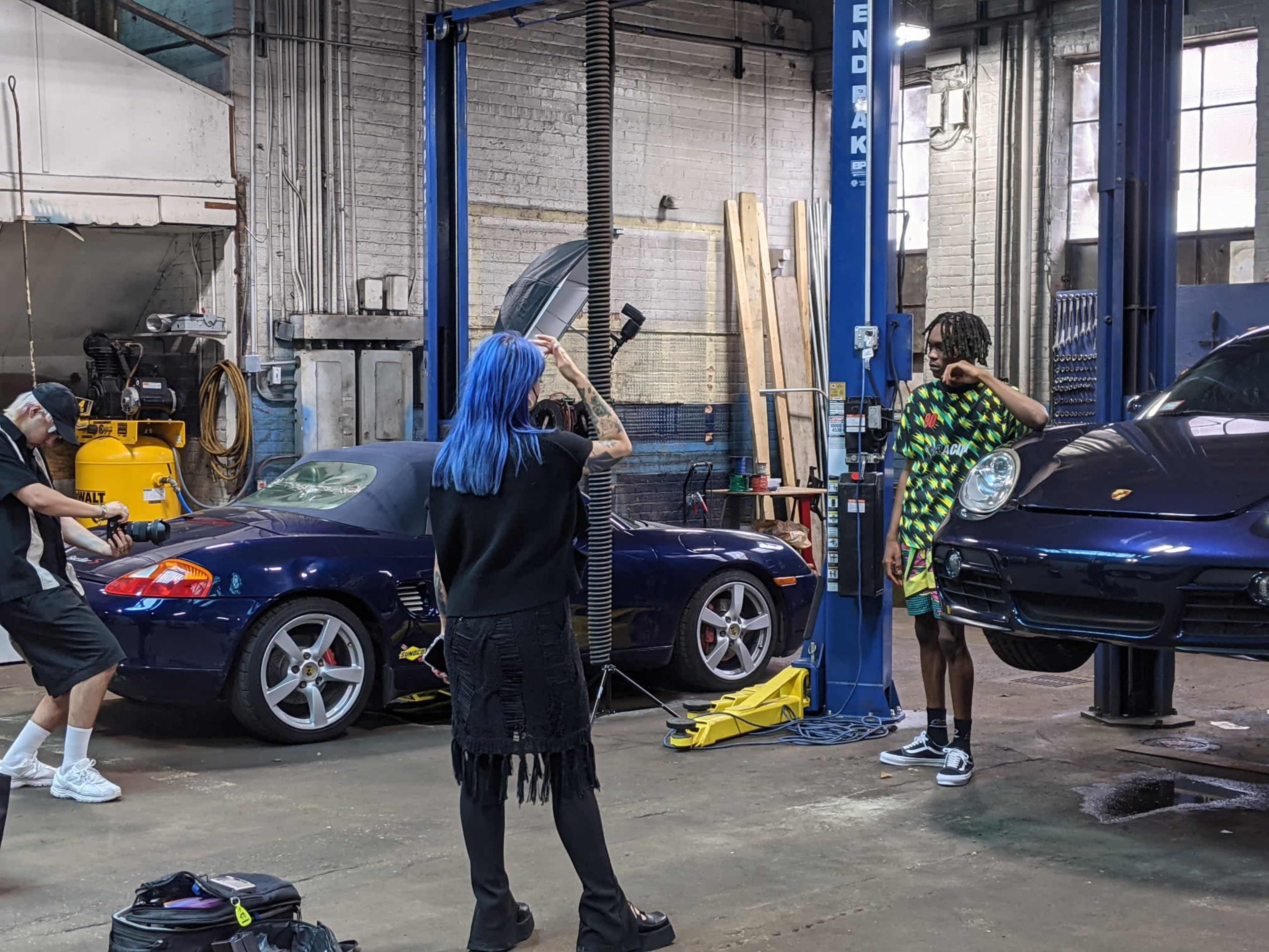A photographer captures a model posing next to two sports cars in an auto shop.