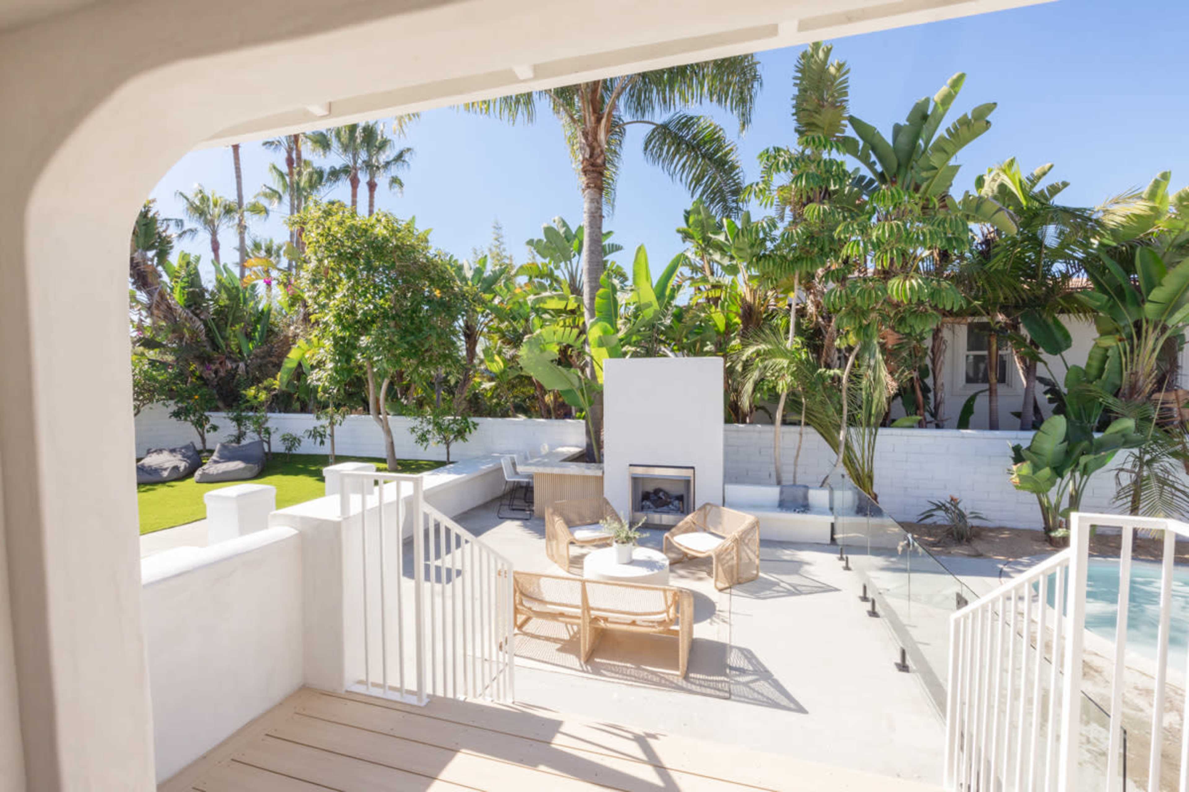 A modern outdoor seating area with a fire pit is surrounded by lush tropical plants and palm trees.
