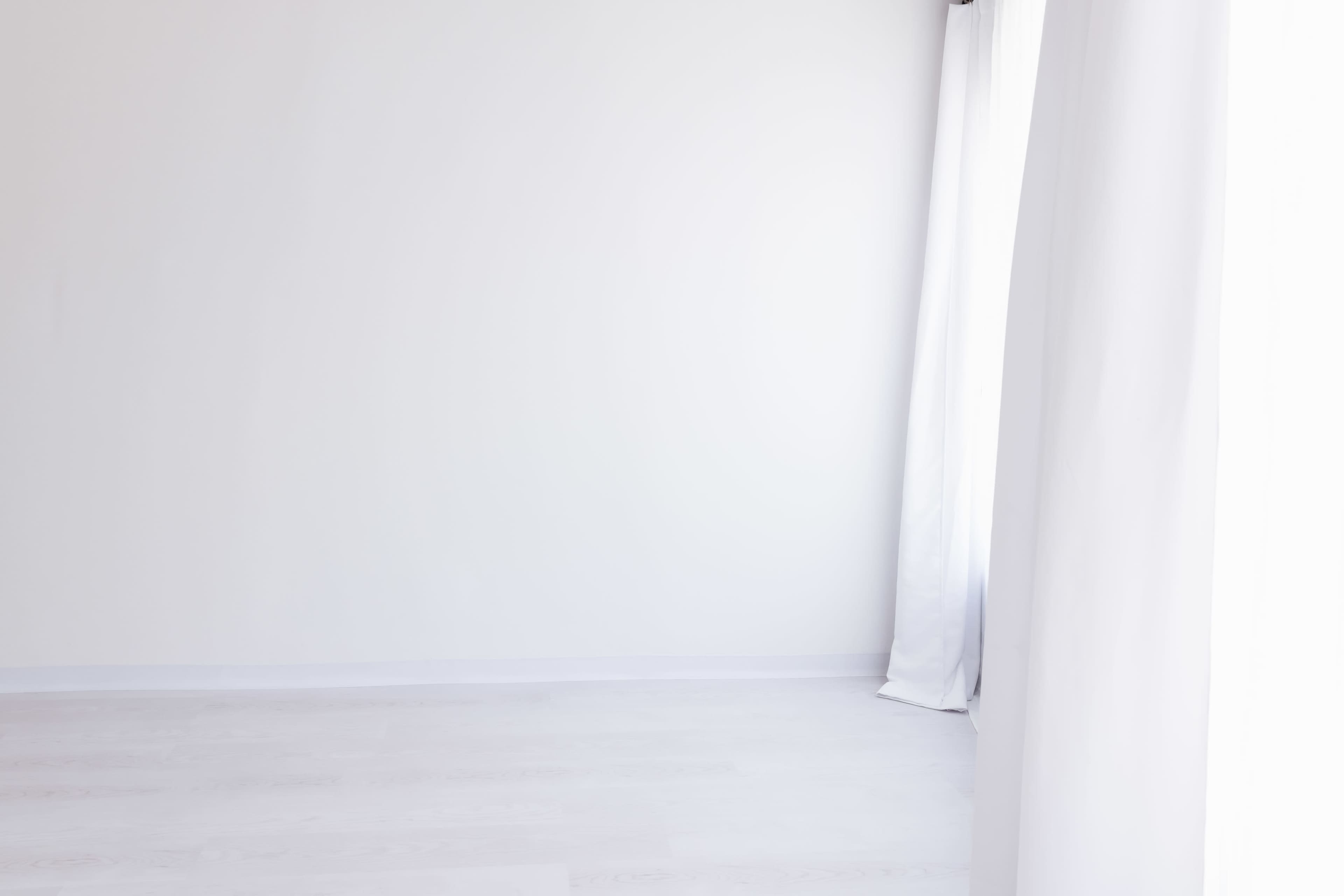 The image shows an empty room with white walls, light-colored flooring, and sheer white curtains.