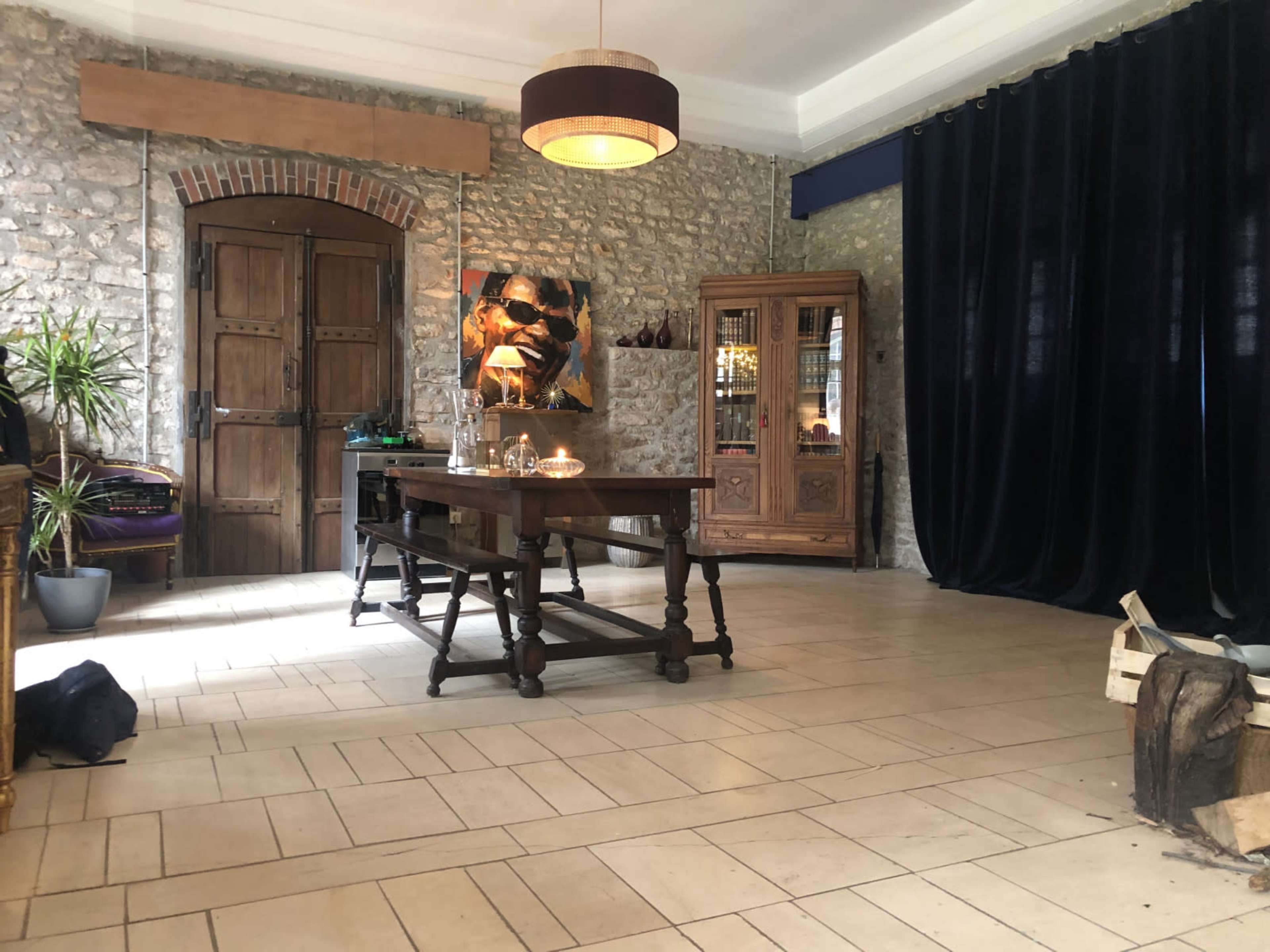 The image shows a spacious interior with stone walls, a wooden table in the center, a cabinet filled with items, and dark curtains on one side.