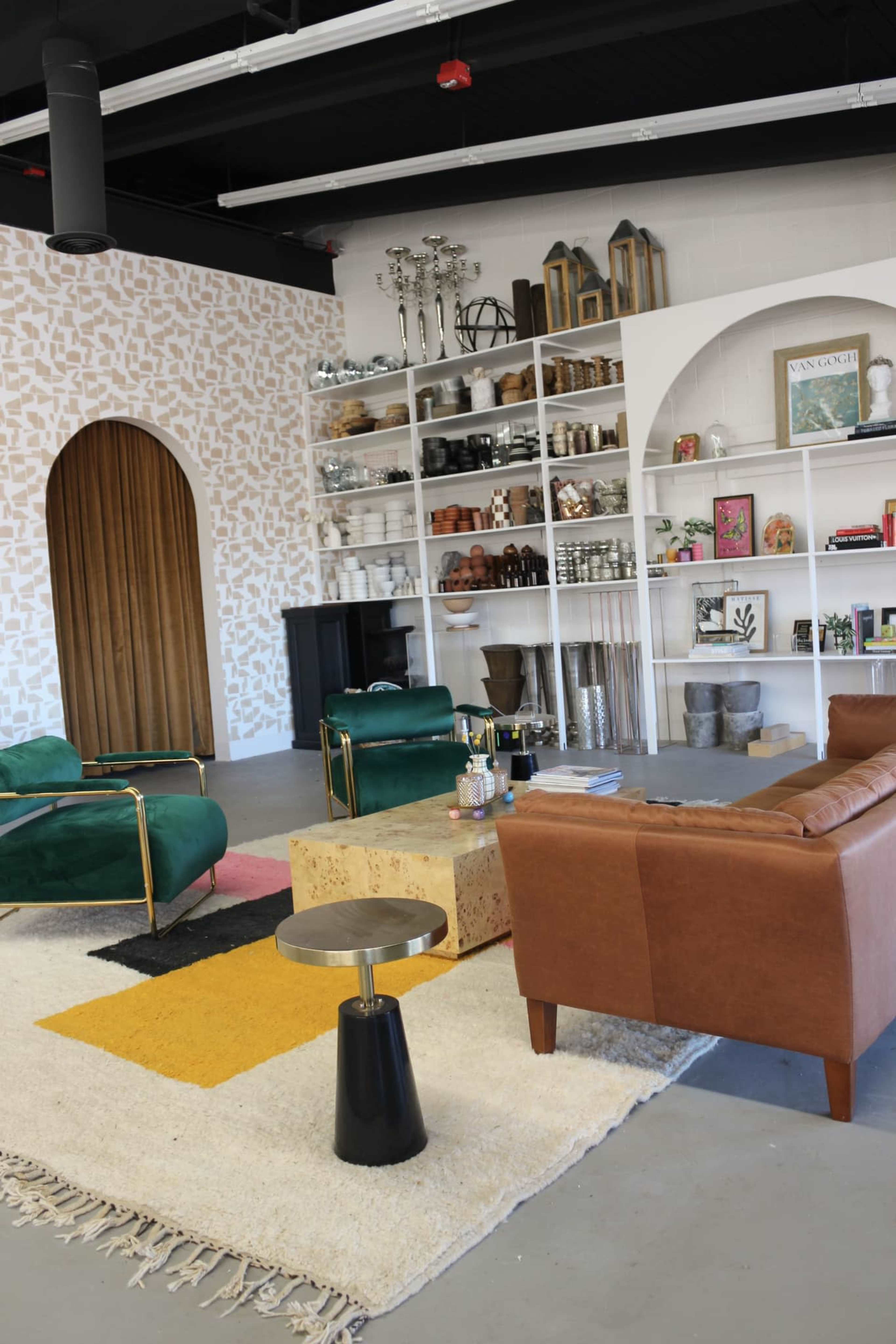 The image shows a modern interior space with a combination of green and brown furniture, a large bookshelf filled with decorative items, and a patterned wall.