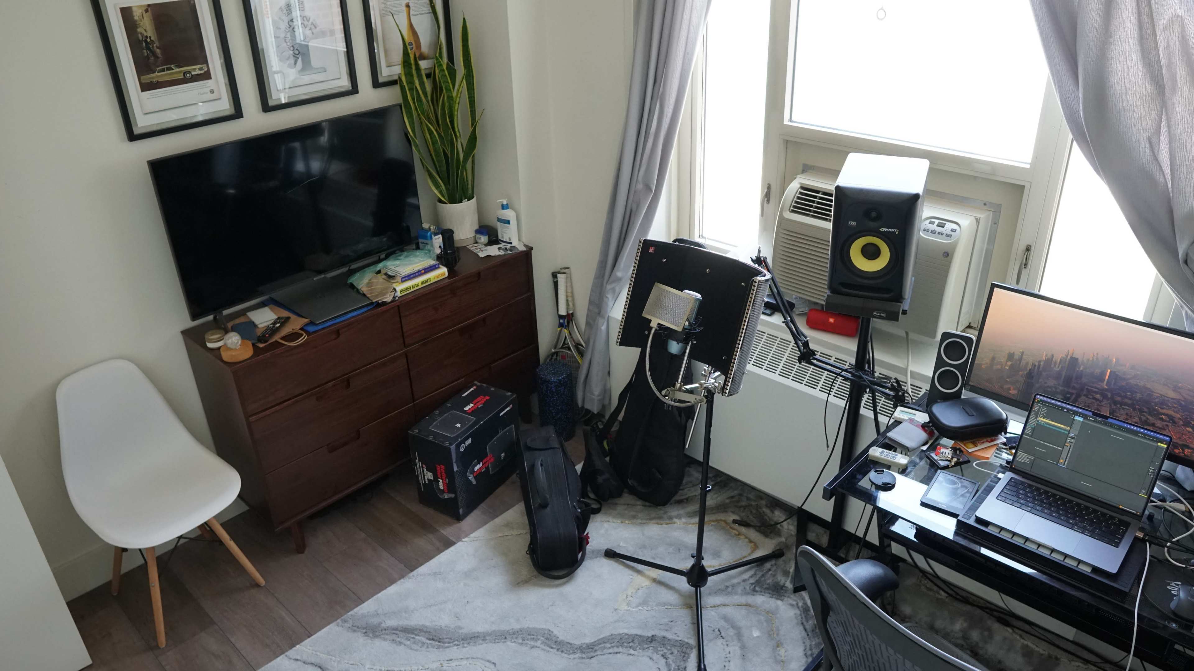 The image shows a small room with a television on a dresser, an air conditioning unit, a computer desk with music production equipment, and a chair in one corner.