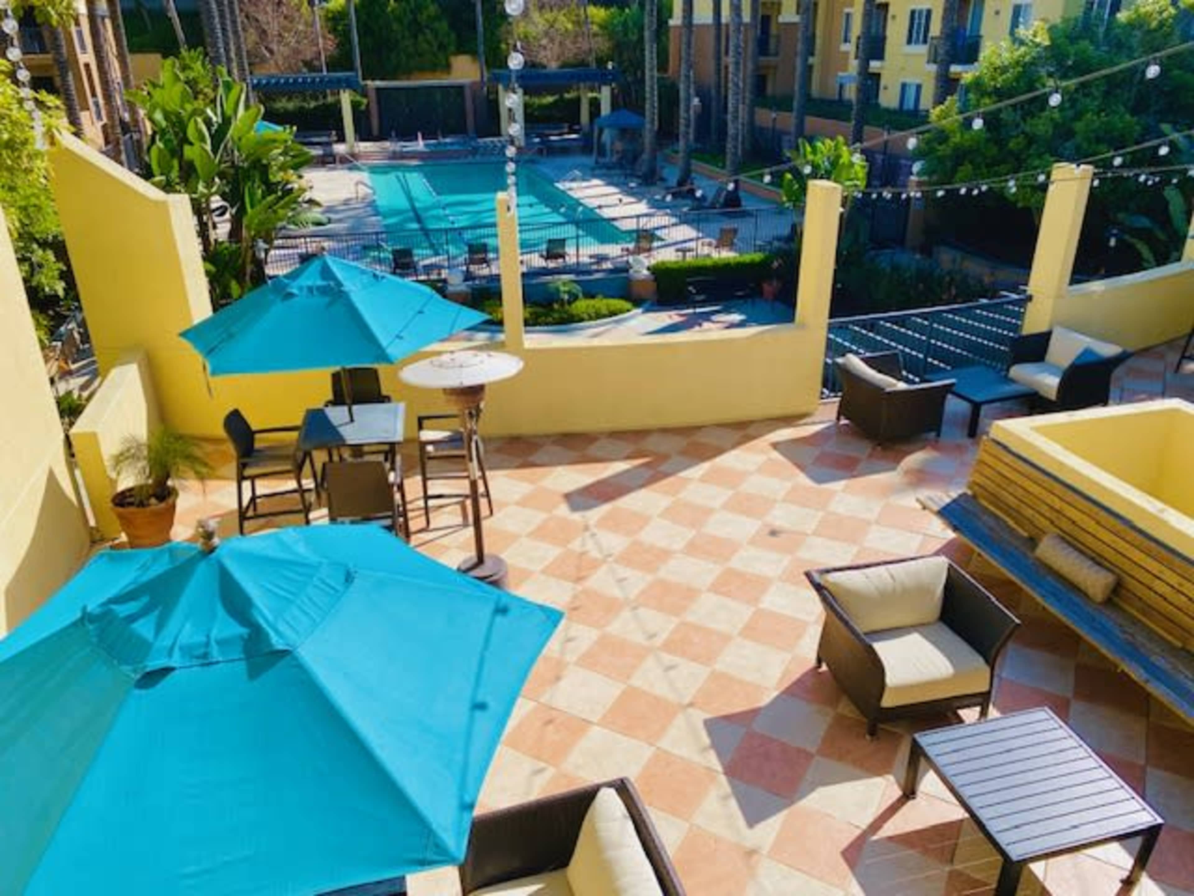 An outdoor lounge area with turquoise umbrellas, seating, and a swimming pool in the background.
