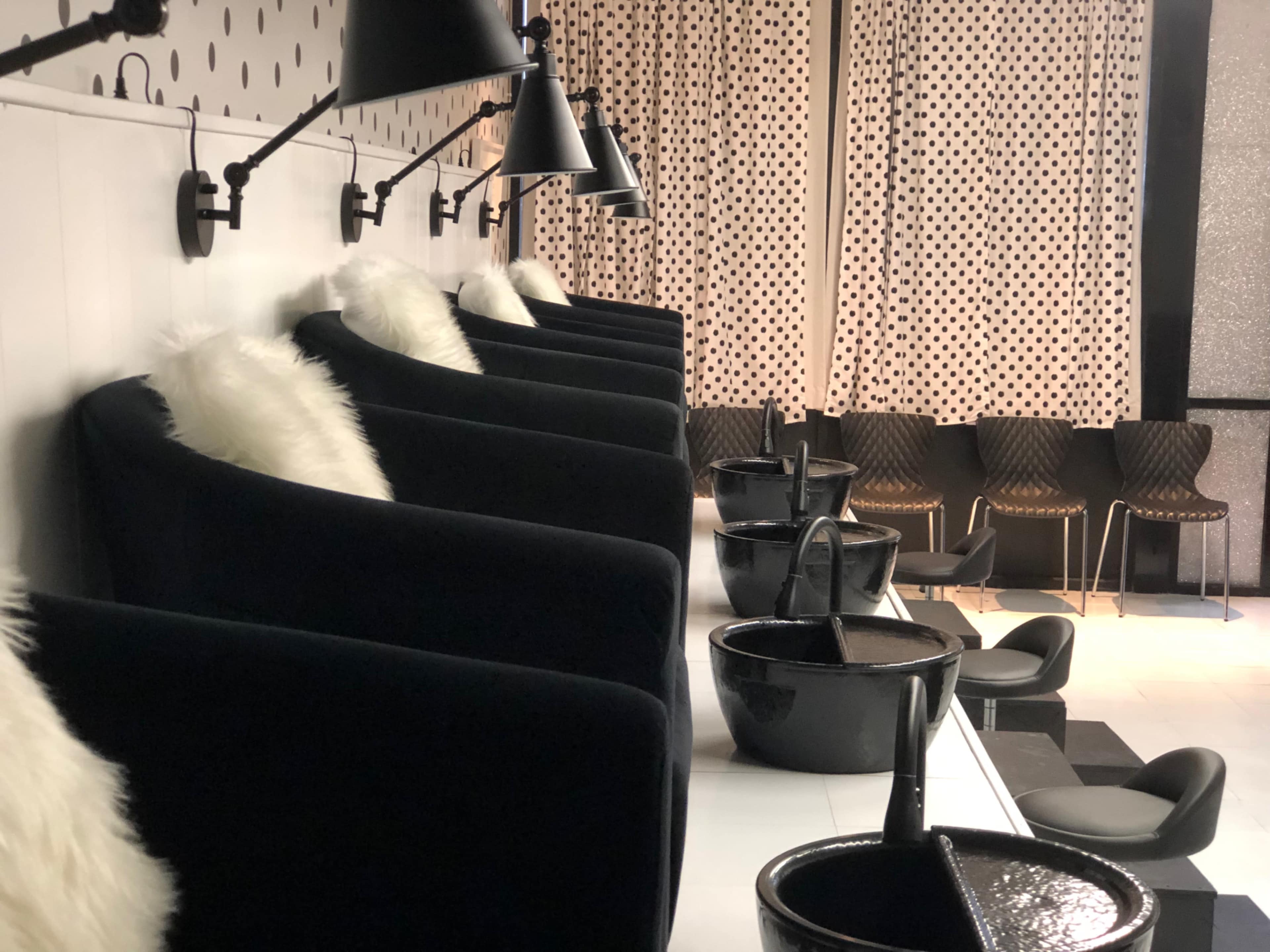 The image shows a modern salon interior with black chairs, wash basins, and decorative curtains featuring a polka dot pattern.