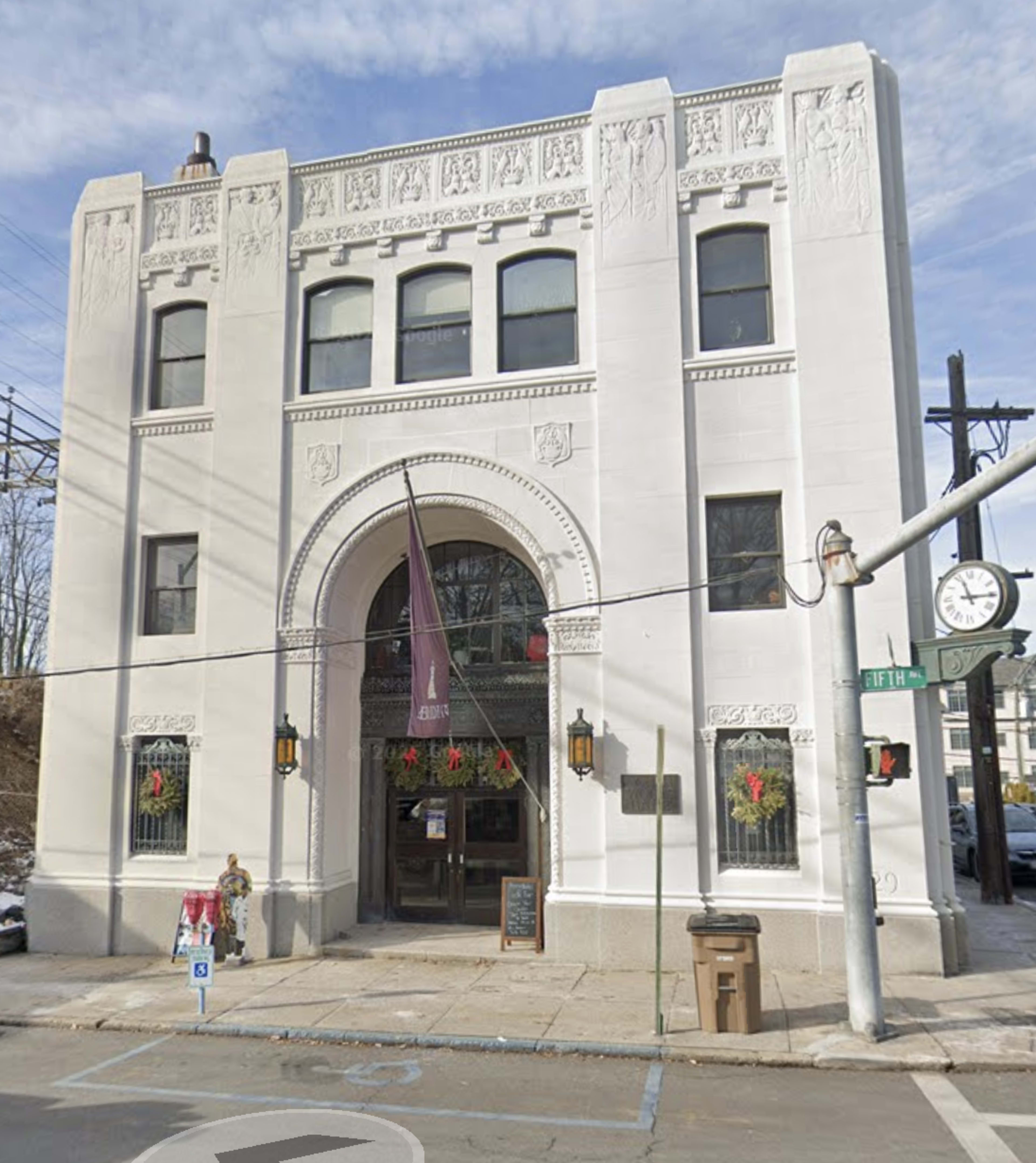 The image shows a prominent, historic building with decorative architectural elements, located on a street corner, featuring a large archway entrance and seasonal decorations.