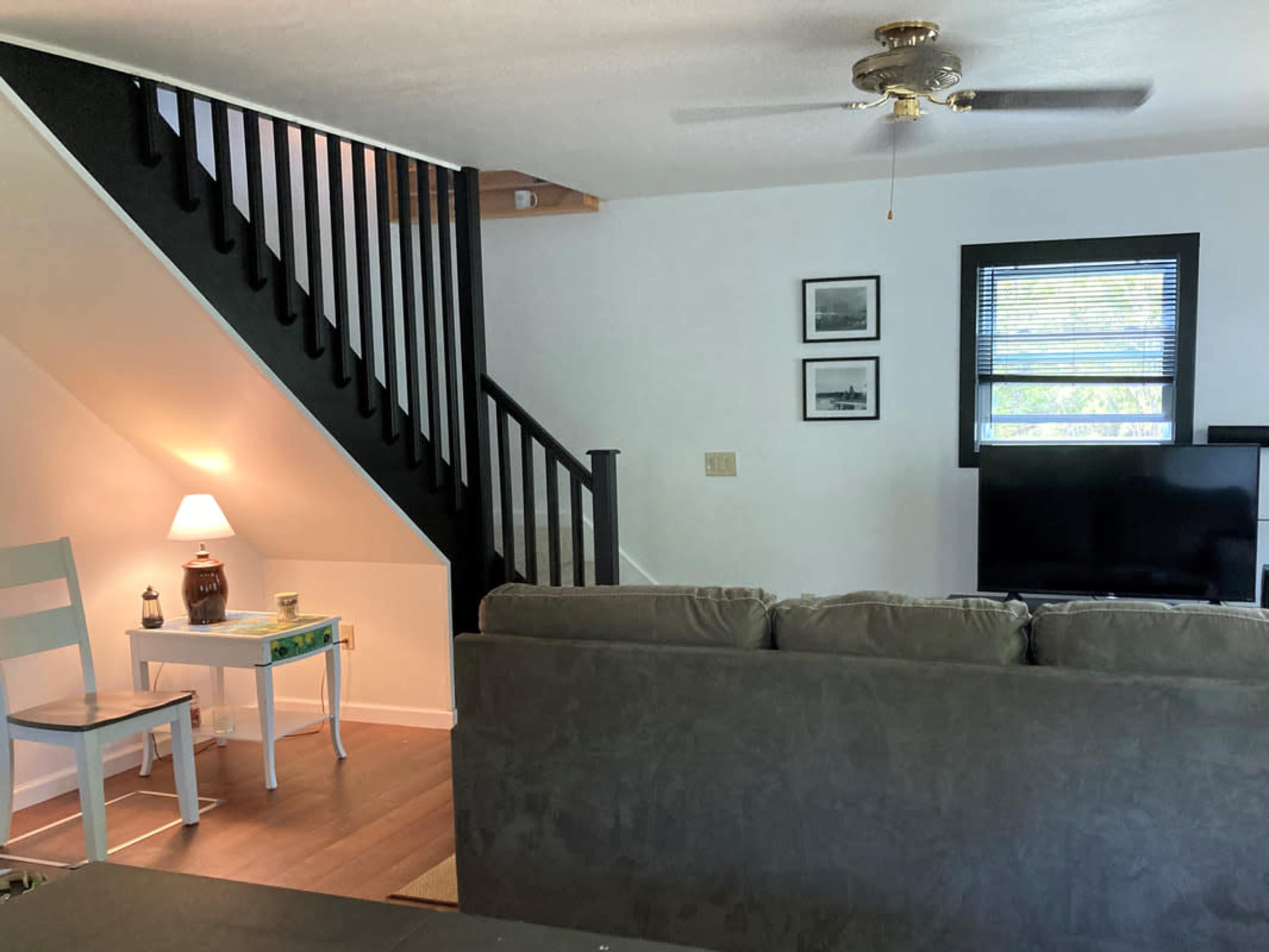 A living room with a couch, a coffee table, a lamp on a side table, and a staircase leading to an upper level.