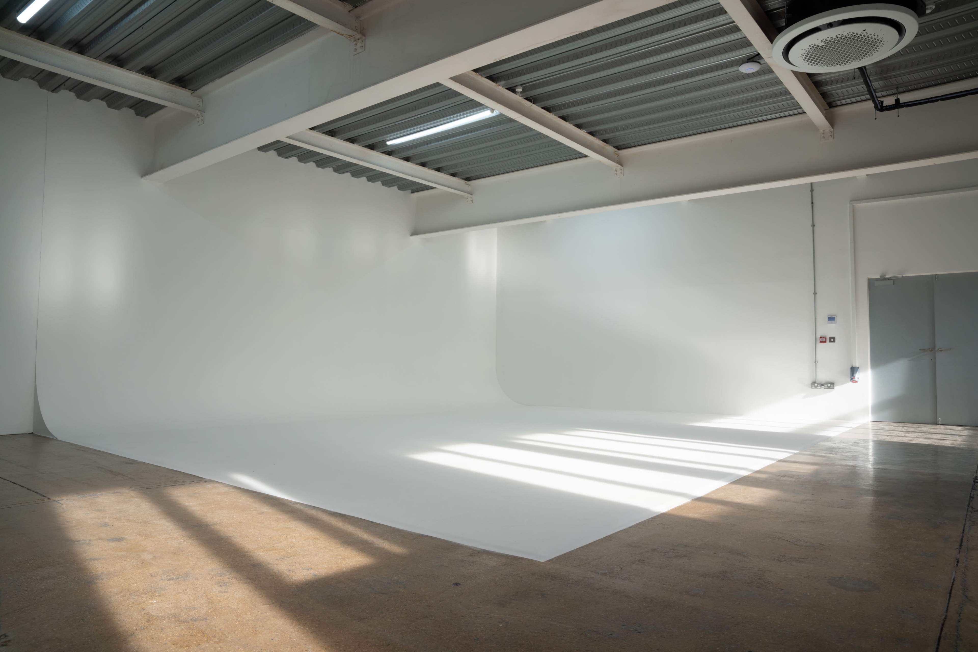 The image shows a spacious, well-lit studio with white walls and a seamless backdrop on the floor.